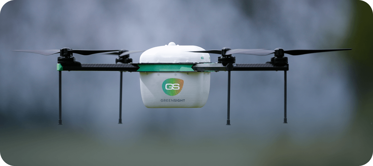 White and black Greesight drone with four propellers flying against a blurred background.