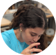 Woman with dark hair wearing a blue shirt drinking from a clear glass.