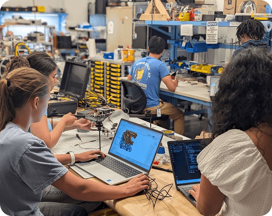 Students collaborate in a workshop setting, working on laptops and assembling a drone prototype.