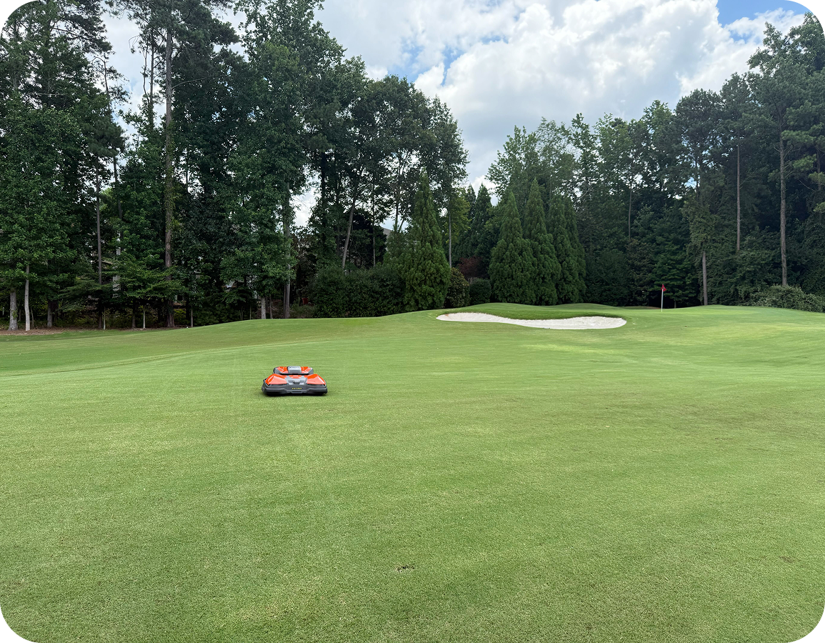 Man standing on grass operating Husqvarna CEORA 546 robotic lawn mower near a golf target flag and a 100-point target board in the background.