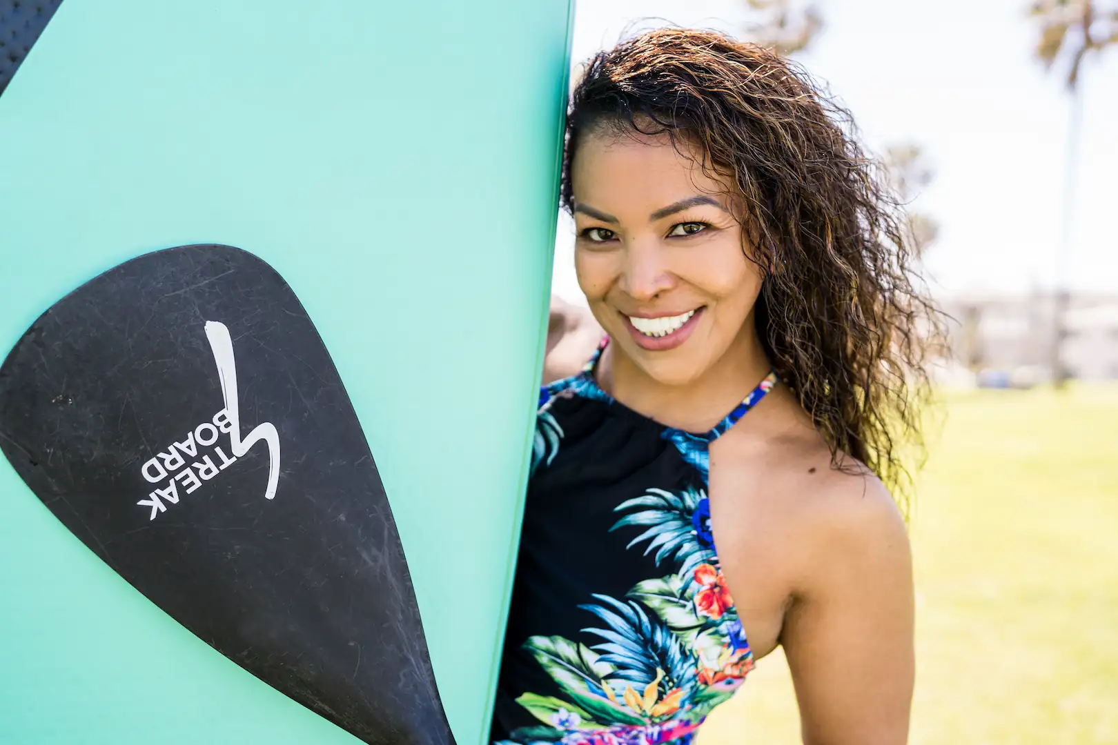 Smiling woman standing outdoors with a paddleboard, showing a bright and confident smile.