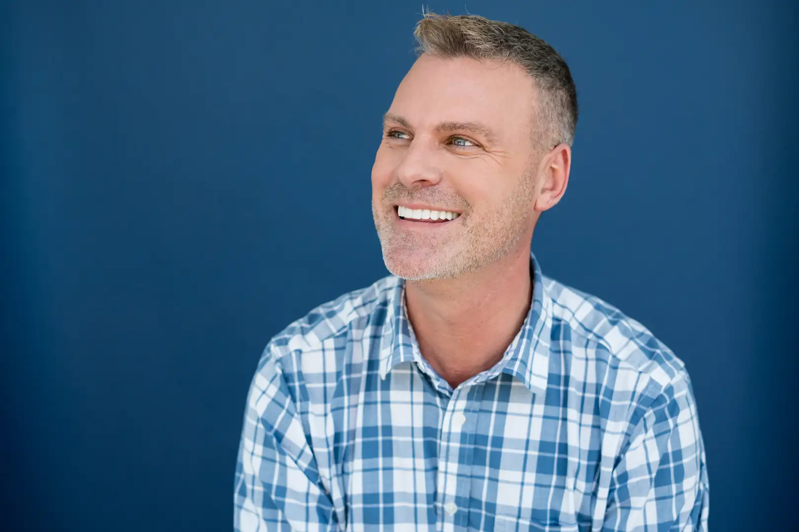 Smiling man in a blue plaid shirt showing his smile makeover from Espire Dental.