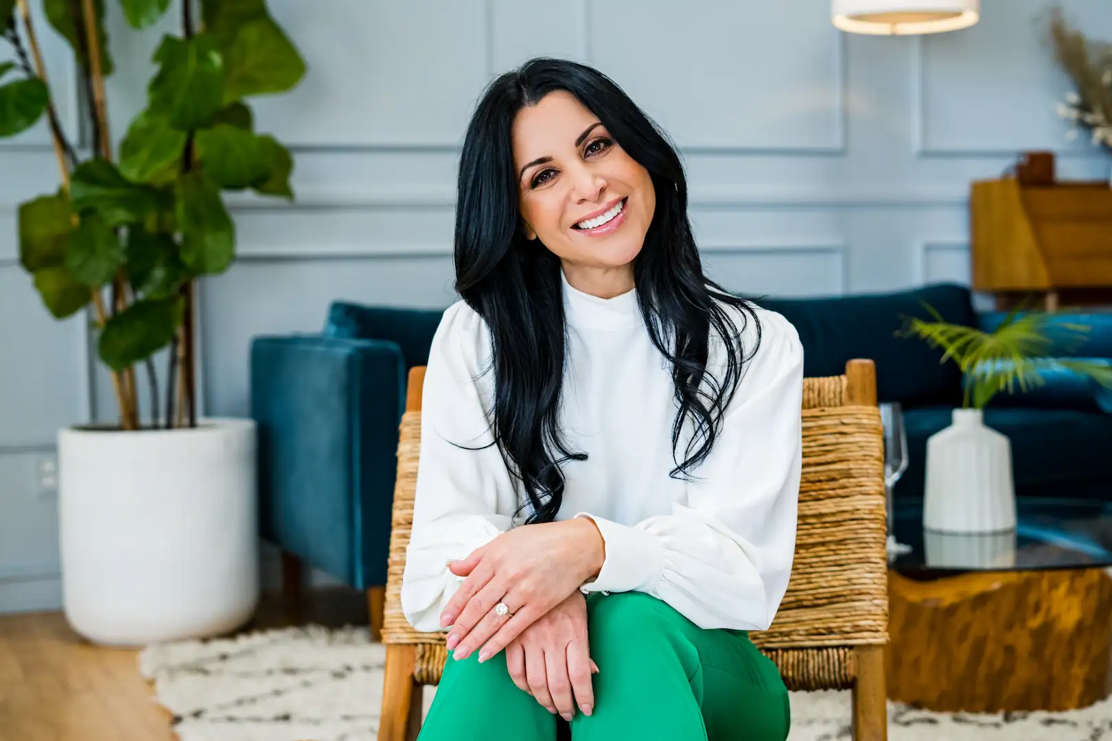 Woman sitting in a modern living space, smiling warmly with a bright, confident smile.