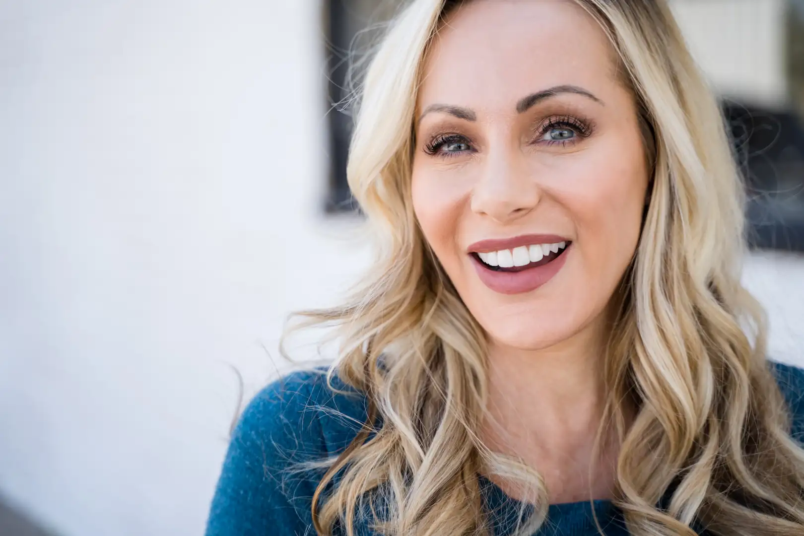 Close-up of a woman with blonde hair smiling brightly and showing her white, healthy teeth.