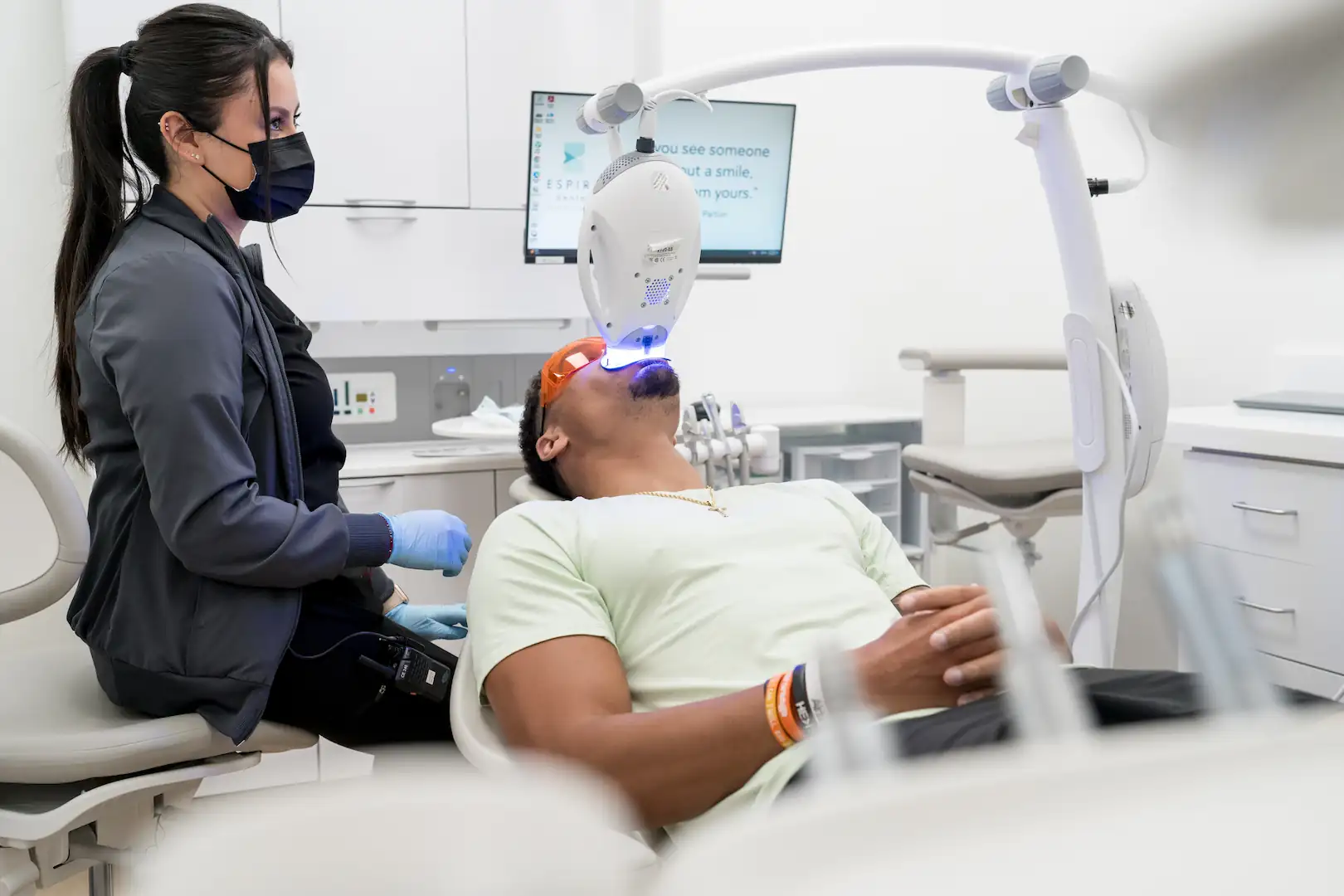 Espire patient receiving professional teeth whitening treatment with a dental assistant monitoring the whitening light in a modern treatment room.