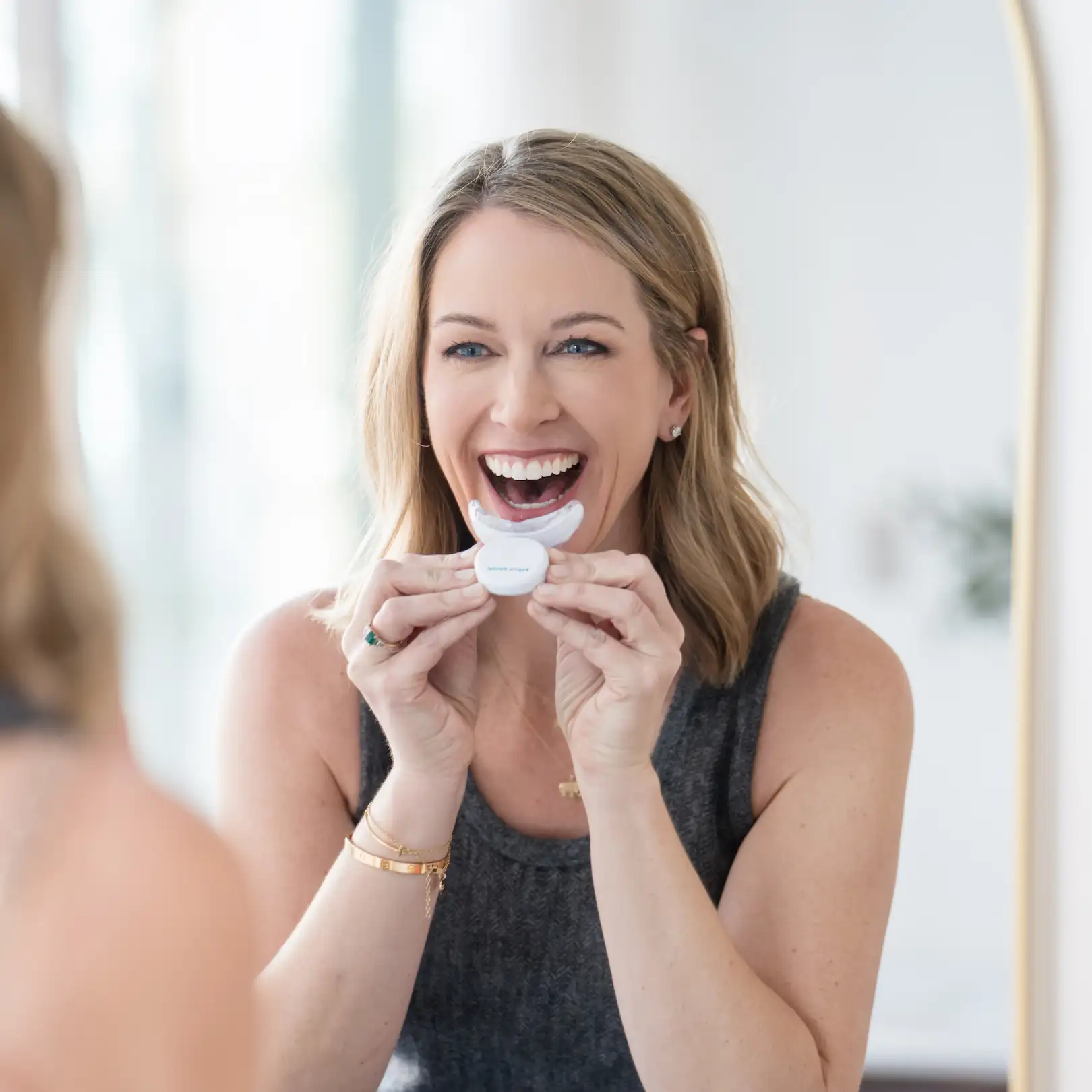 Smiling Espire patient holding an at-home teeth whitening device while looking in the mirror, showing a bright and confident smile.