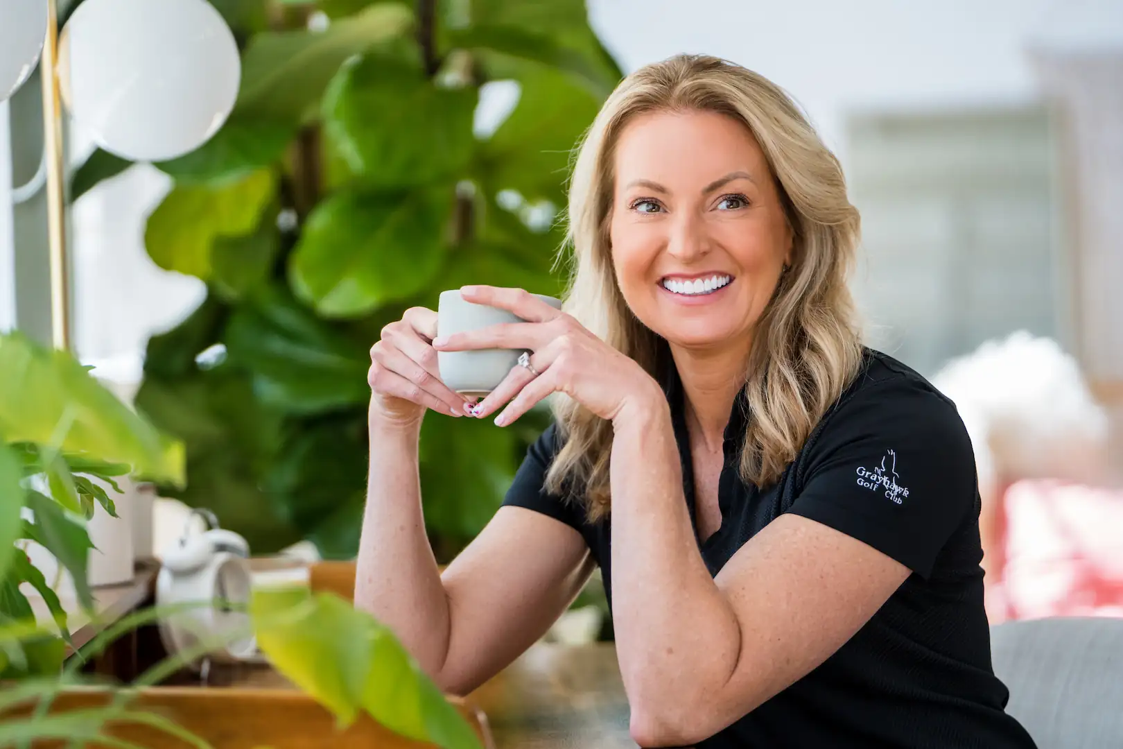 Smiling Espire patient holding a cup of coffee while sitting indoors surrounded by plants, showing a bright and healthy smile.