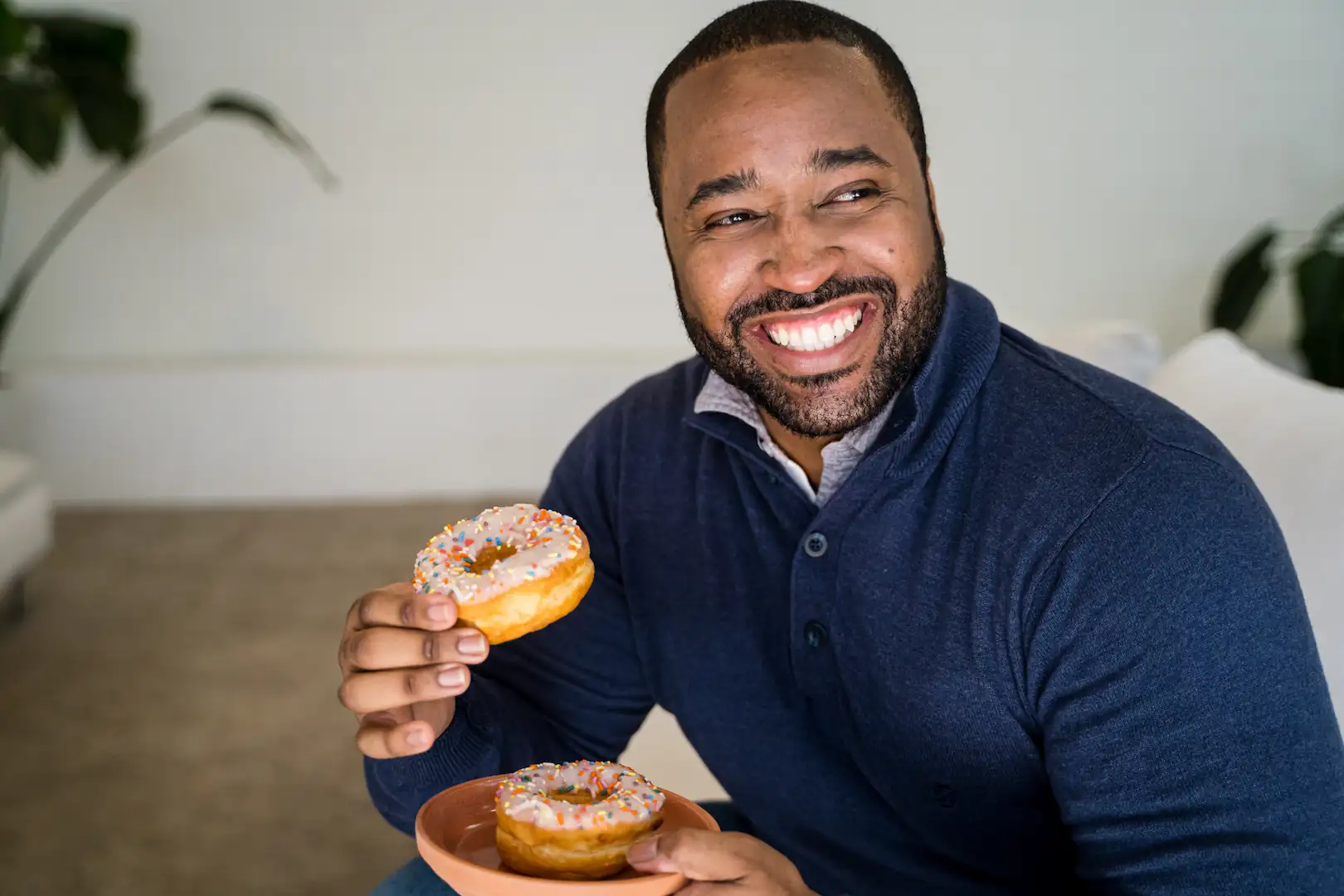 Smiling Espire patient holding two sprinkled donuts while seated indoors, showing a confident and healthy smile.