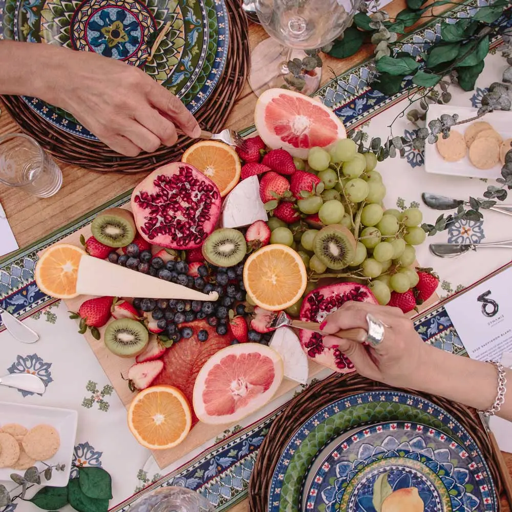 Vibrant fruit platter with grapes, oranges, pomegranate, kiwi, and strawberries on a decorative table setting.