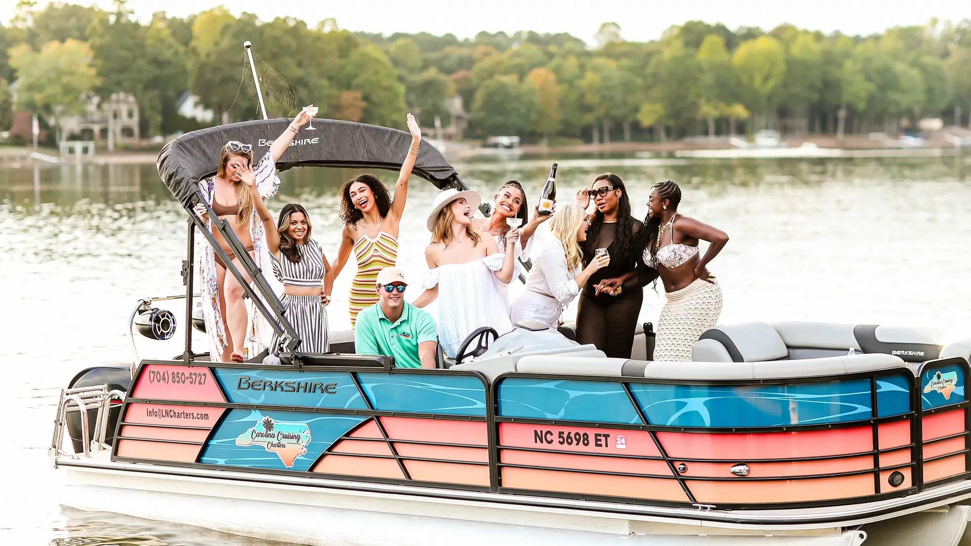 Group celebrating on a boat, holding drinks, with trees in the background, festive atmosphere, lake setting.