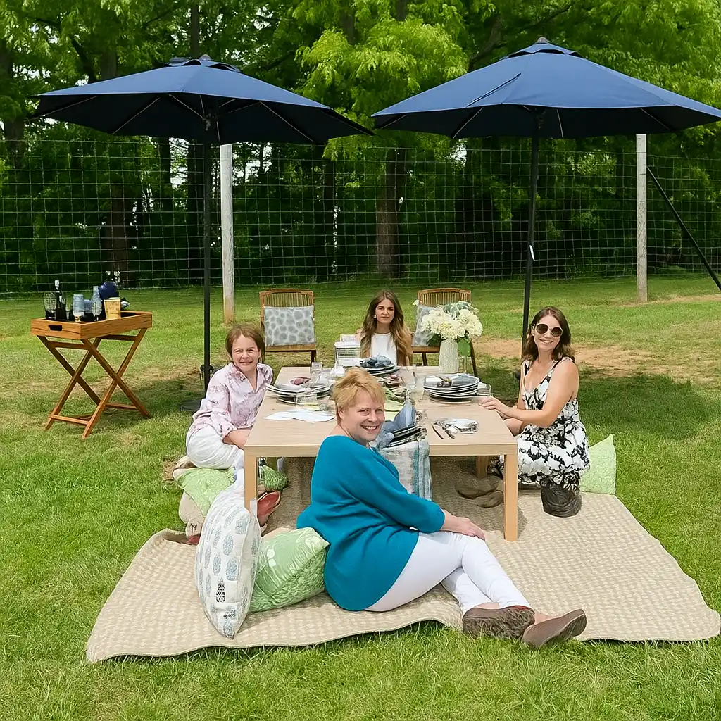 Four people enjoying an outdoor picnic under umbrellas, surrounded by trees and a well-set table.
