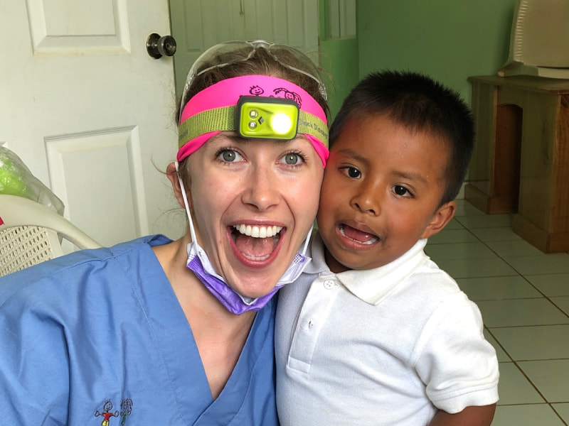 An enthusiastic Espire Dental team member in scrubs and a headlamp smiles with a young child during an outreach event, representing the impact of Espire Dental’s Whitening for Charity program.