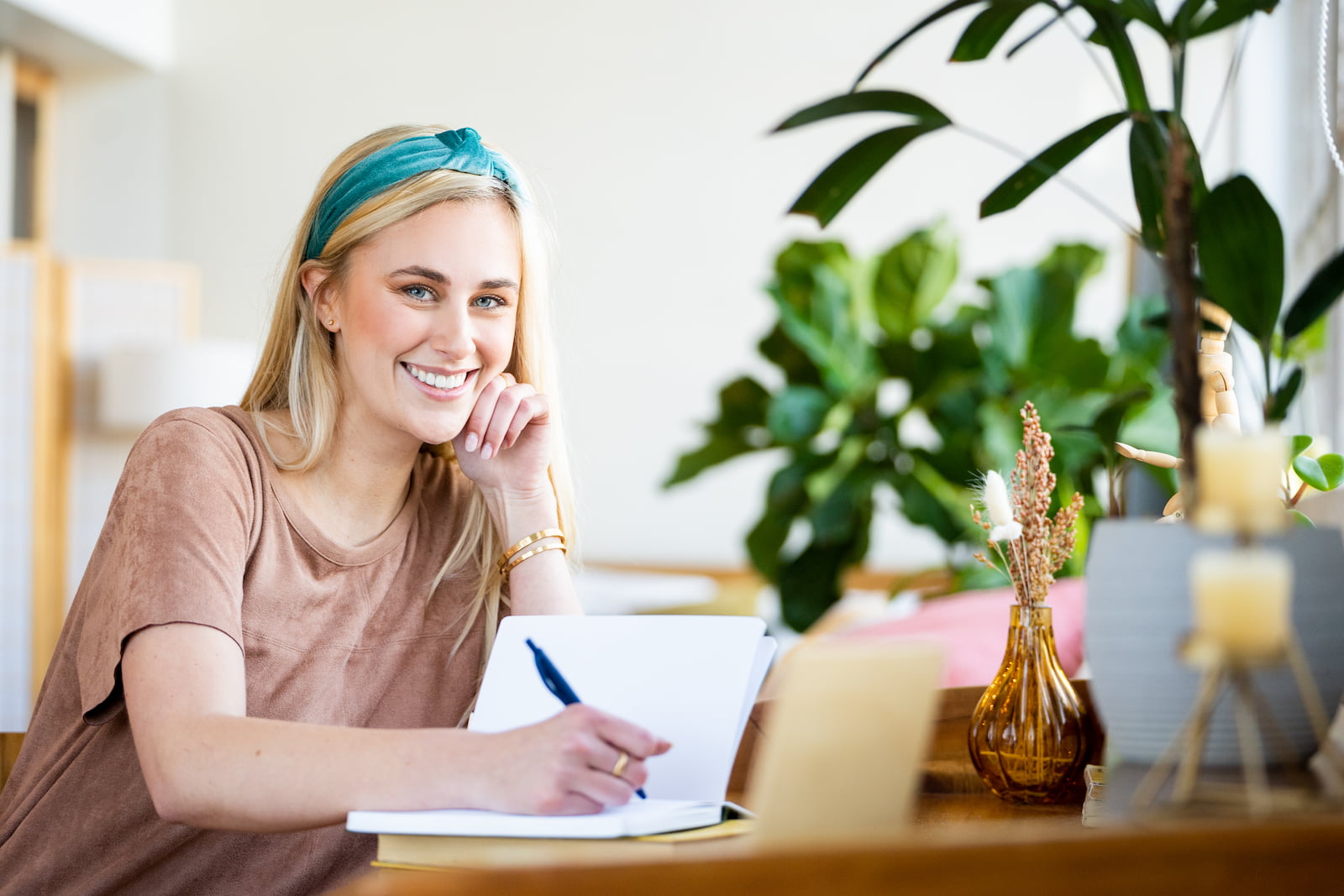 Smiling Espire Dental La Jolla patient showing off her new smile makeover while sitting at a desk with a notebook, wearing a teal headband and looking relaxed in a bright, modern space.