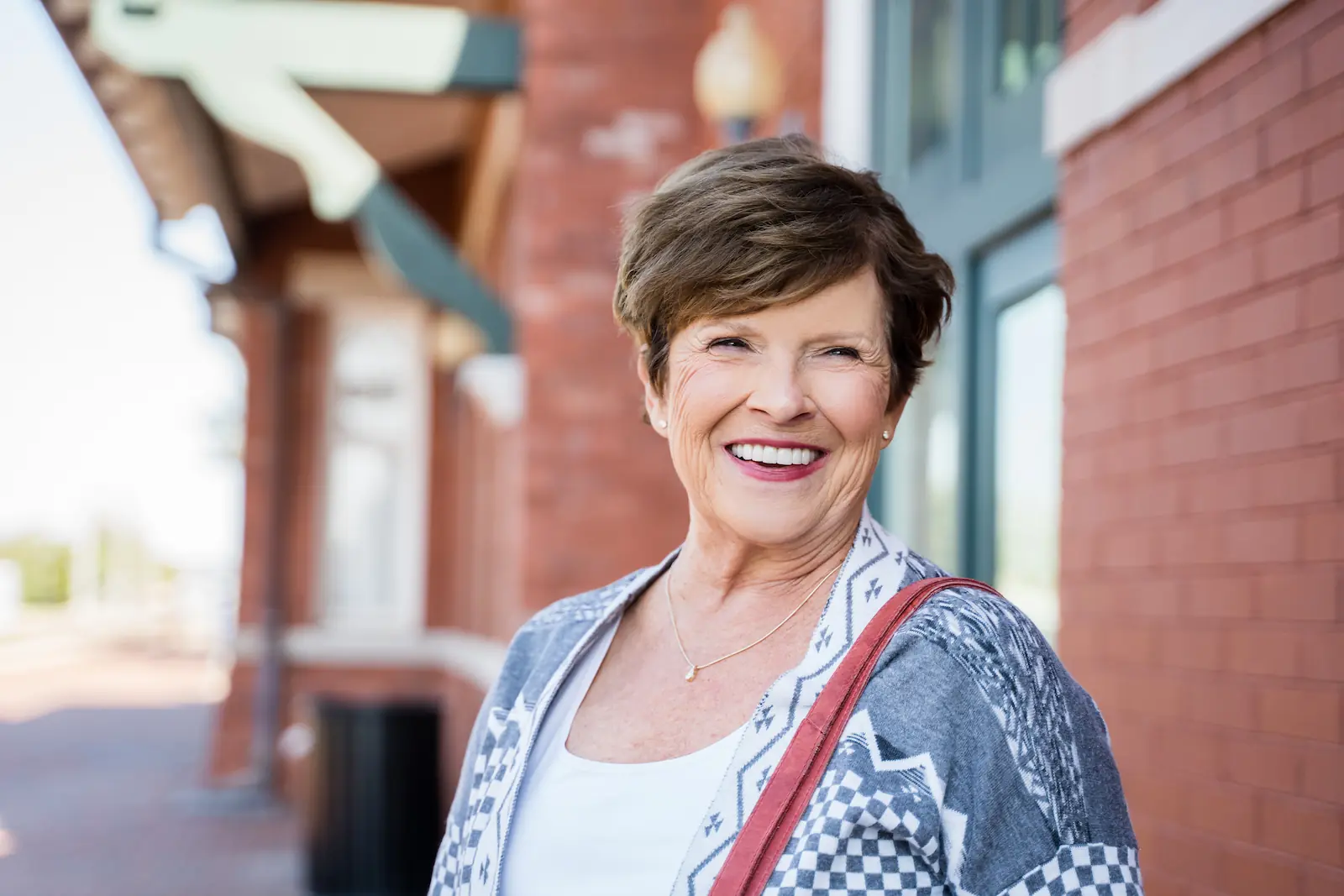 Senior woman smiling confidently outside a brick building after visiting Espire Dental