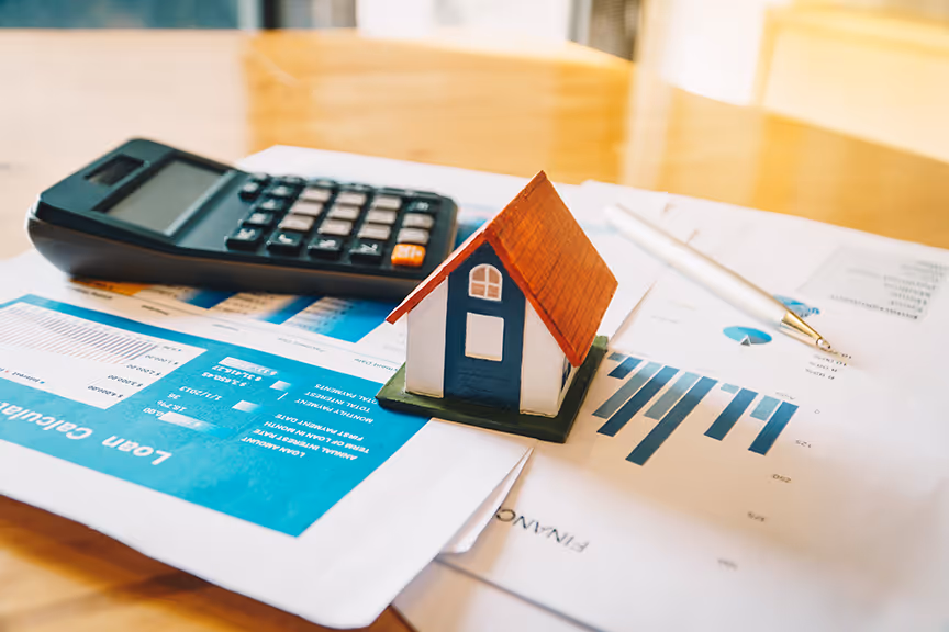 A house model sitting on top of a table next to a calculator.