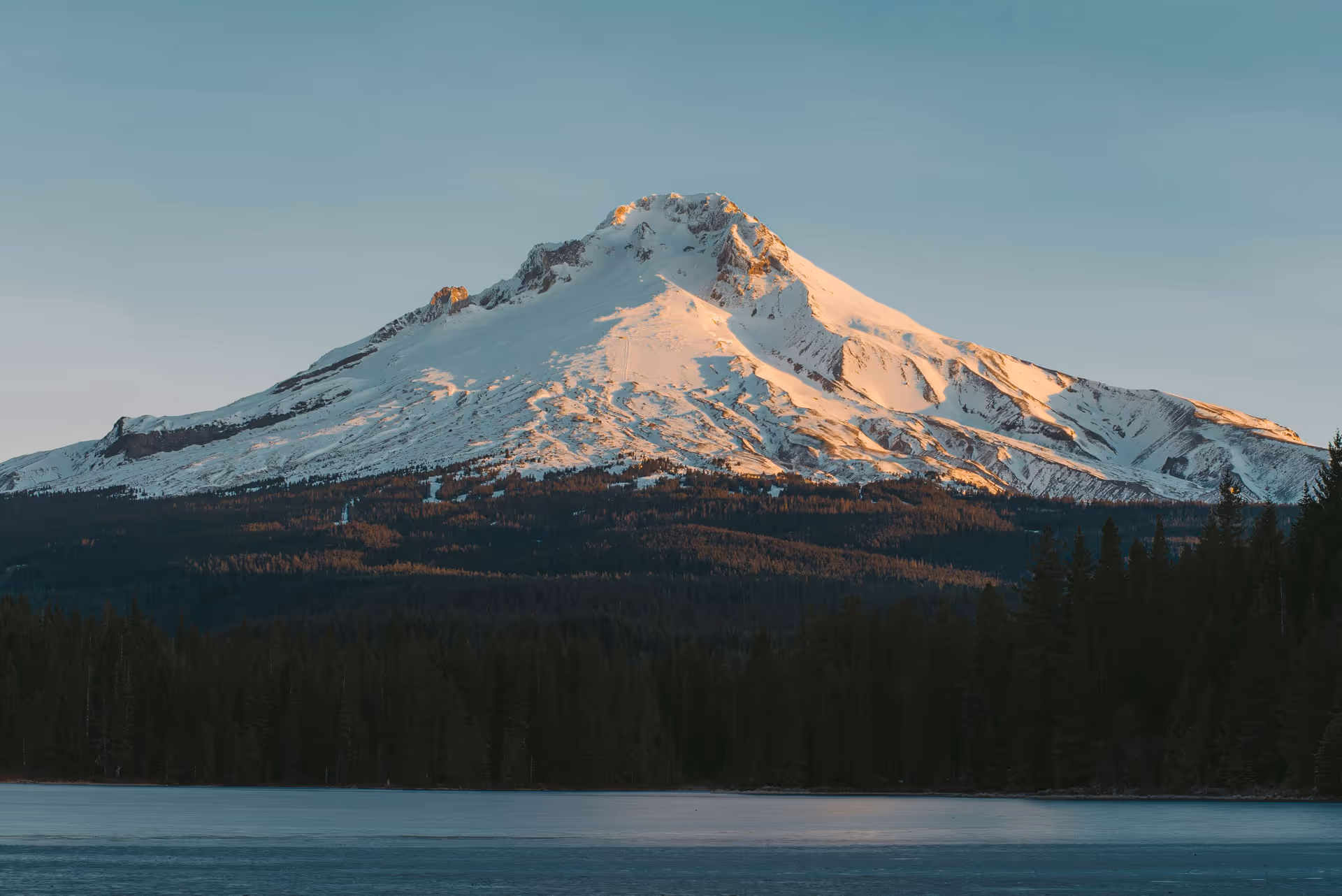 A large snow covered mountain towering over a lake.