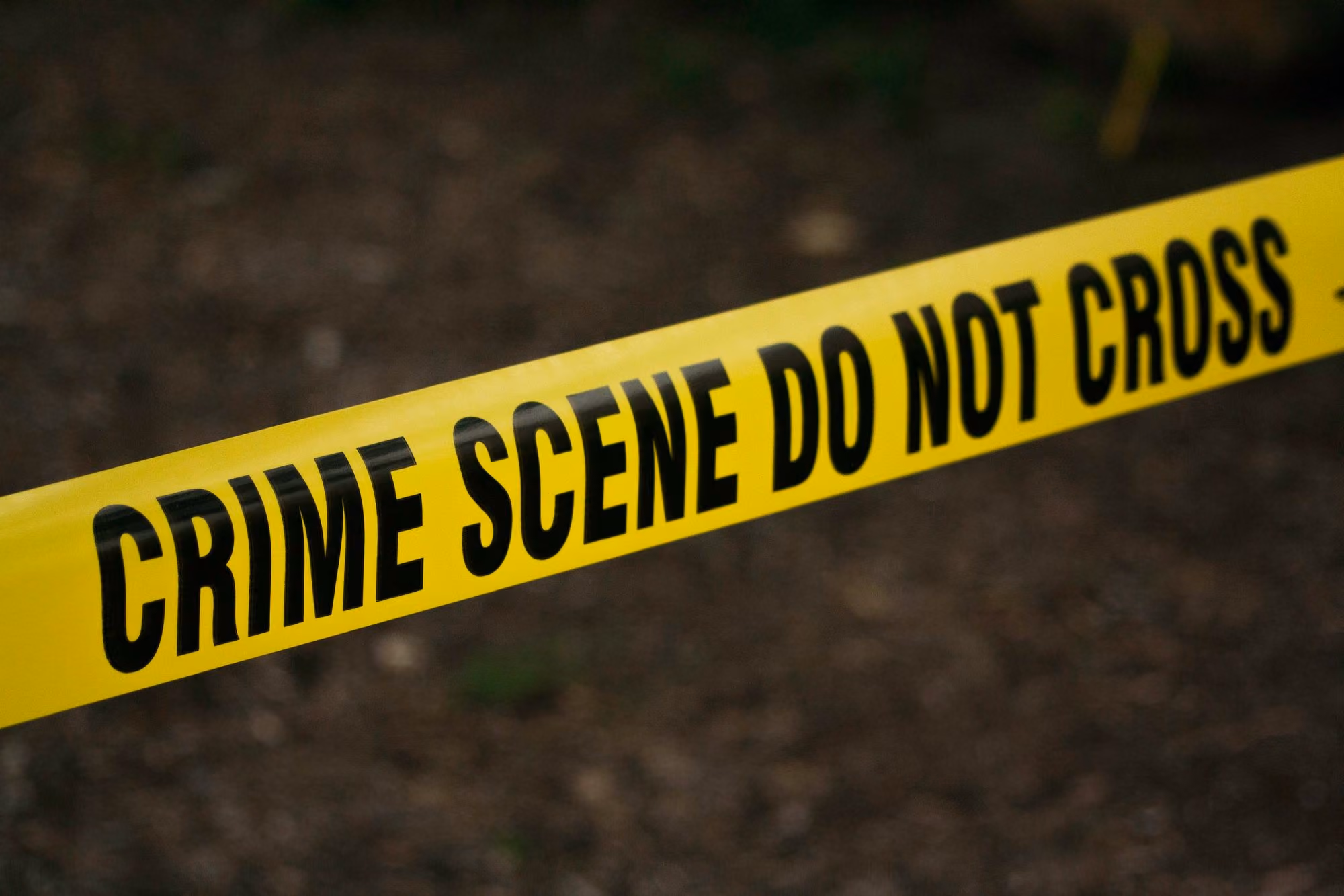 Yellow crime scene tape with black warning text stretched across a blurred outdoor background.