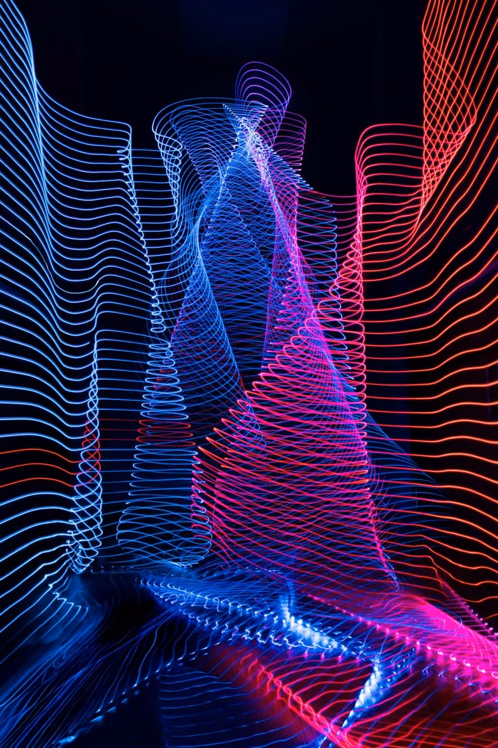 Abstract swirling neon light trails in blue, purple, pink, and red on a black background.