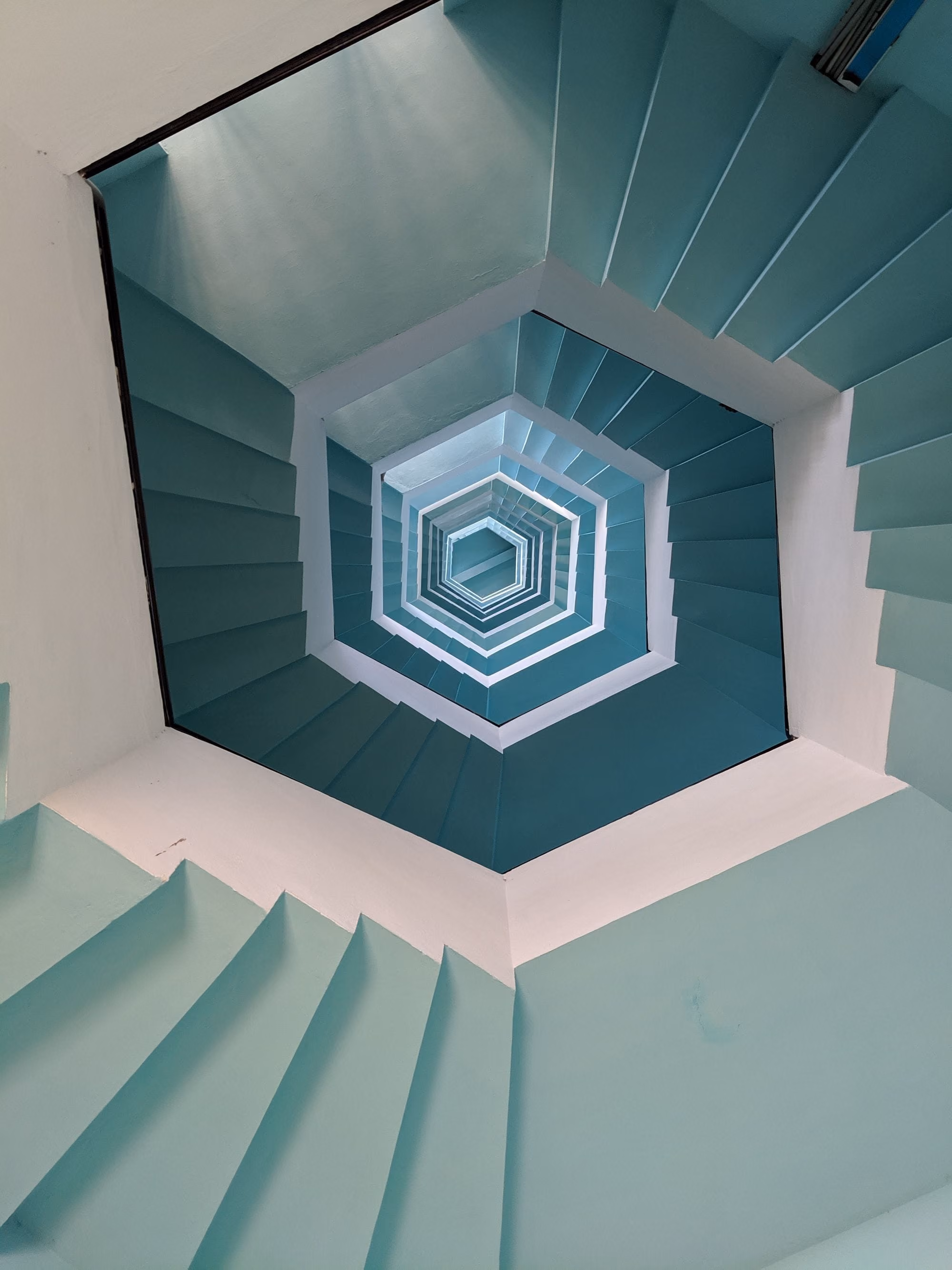 View looking up at a hexagonal spiral staircase painted in shades of blue and white.