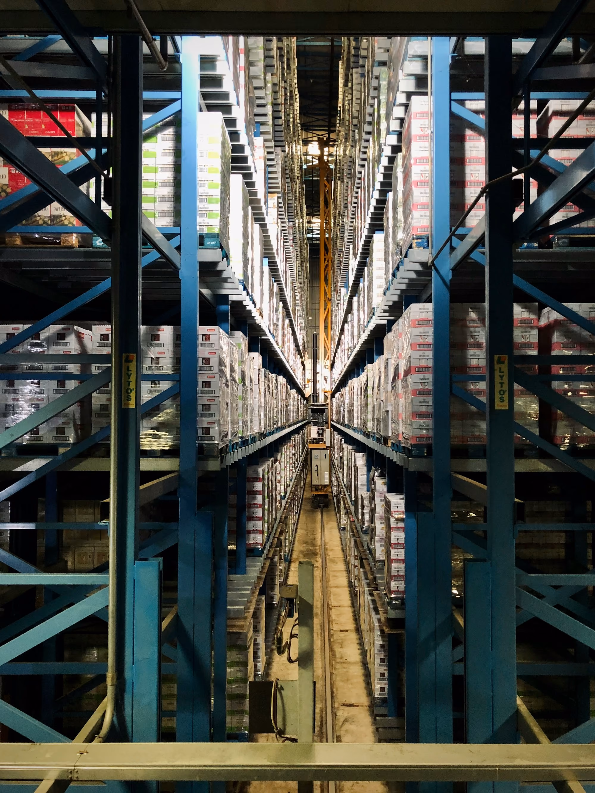 Long aisle in warehouse with tall blue metal shelves stacked with boxes on both sides.