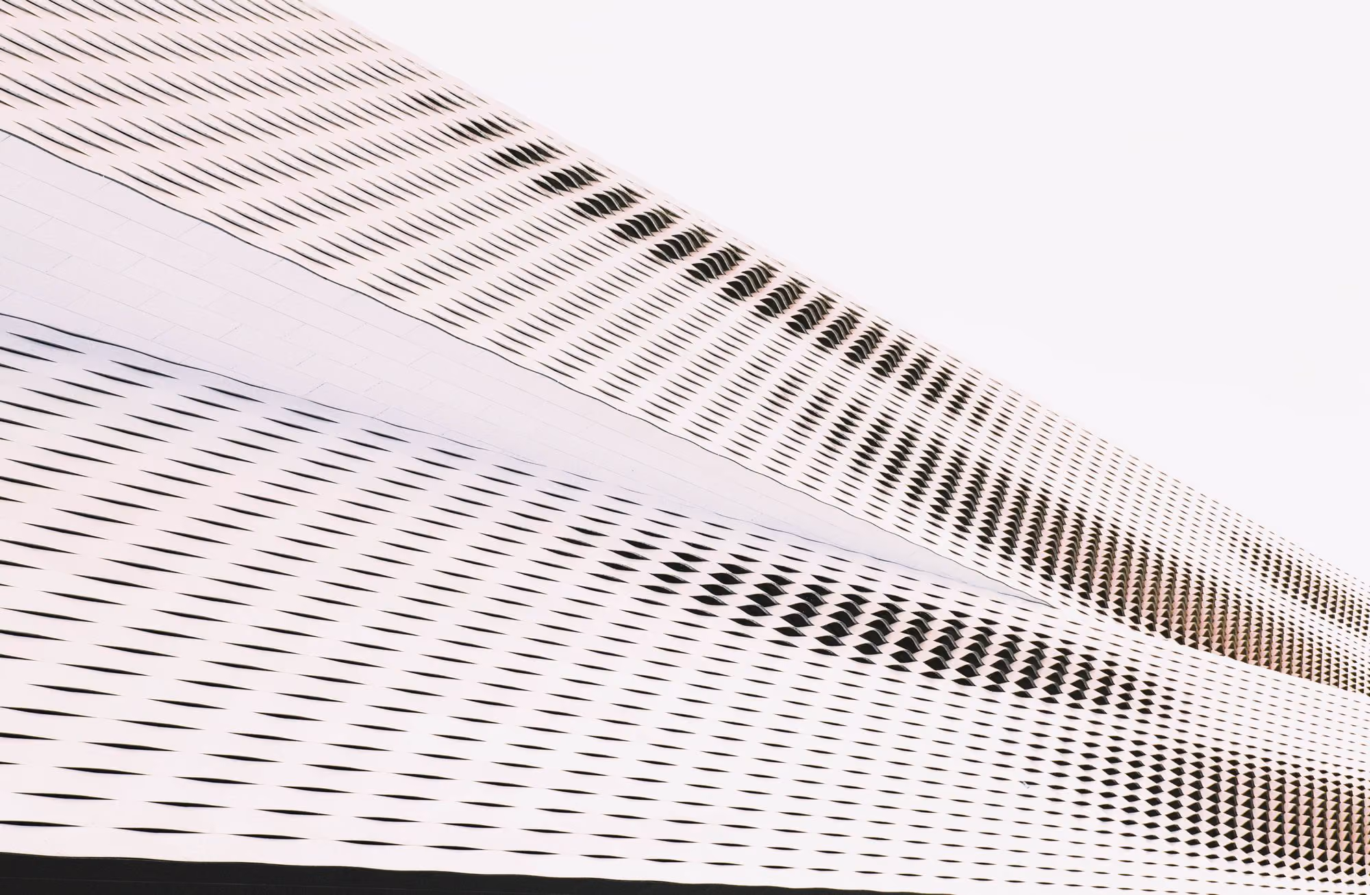 Curved modern building facade with repeating black diagonal slits on white panels.