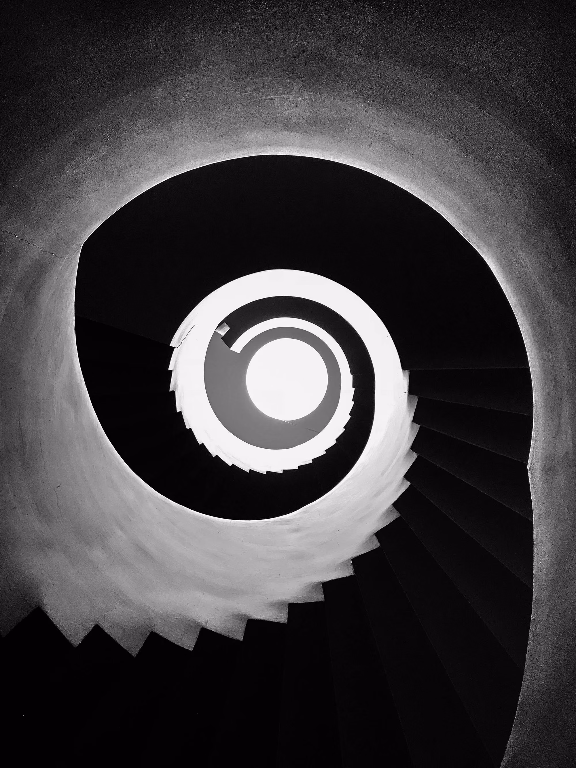 Black and white photo looking up inside a spiral staircase with a bright circular light at the top.