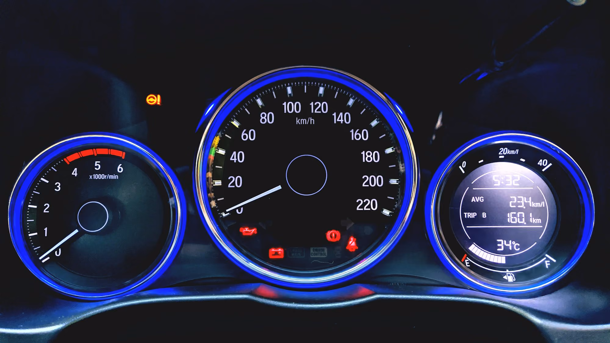 Car dashboard with illuminated speedometer, tachometer, fuel gauge, and warning lights at night.