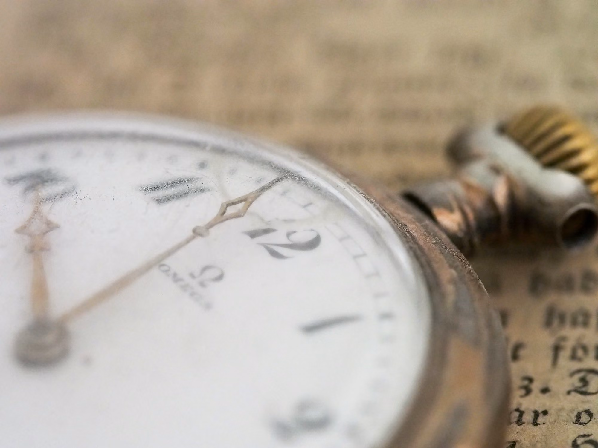 Close-up of an antique Omega pocket watch resting on aged, printed paper.