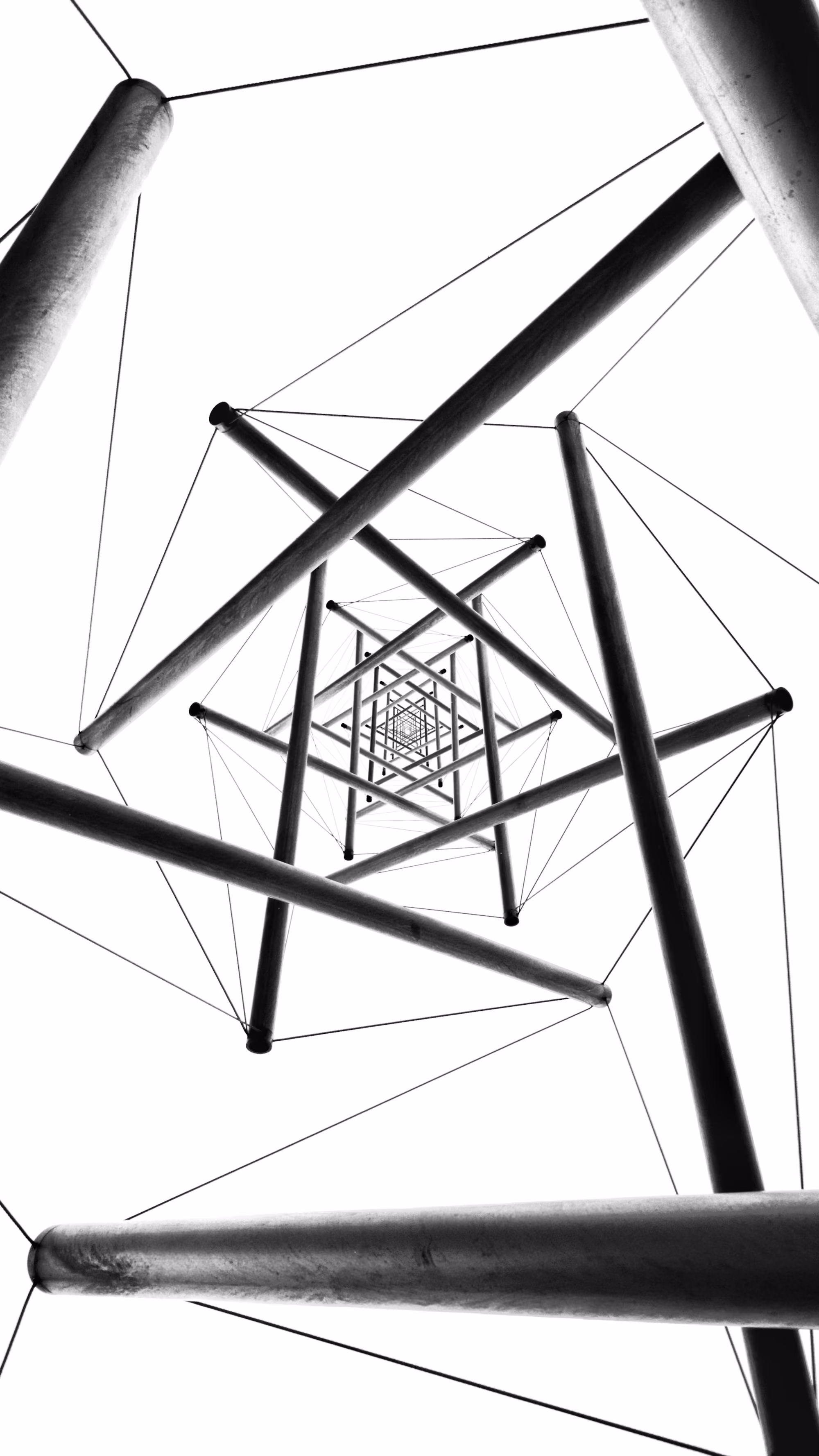 Looking upward inside a tall metal tower with intersecting beams and tension cables in black and white.