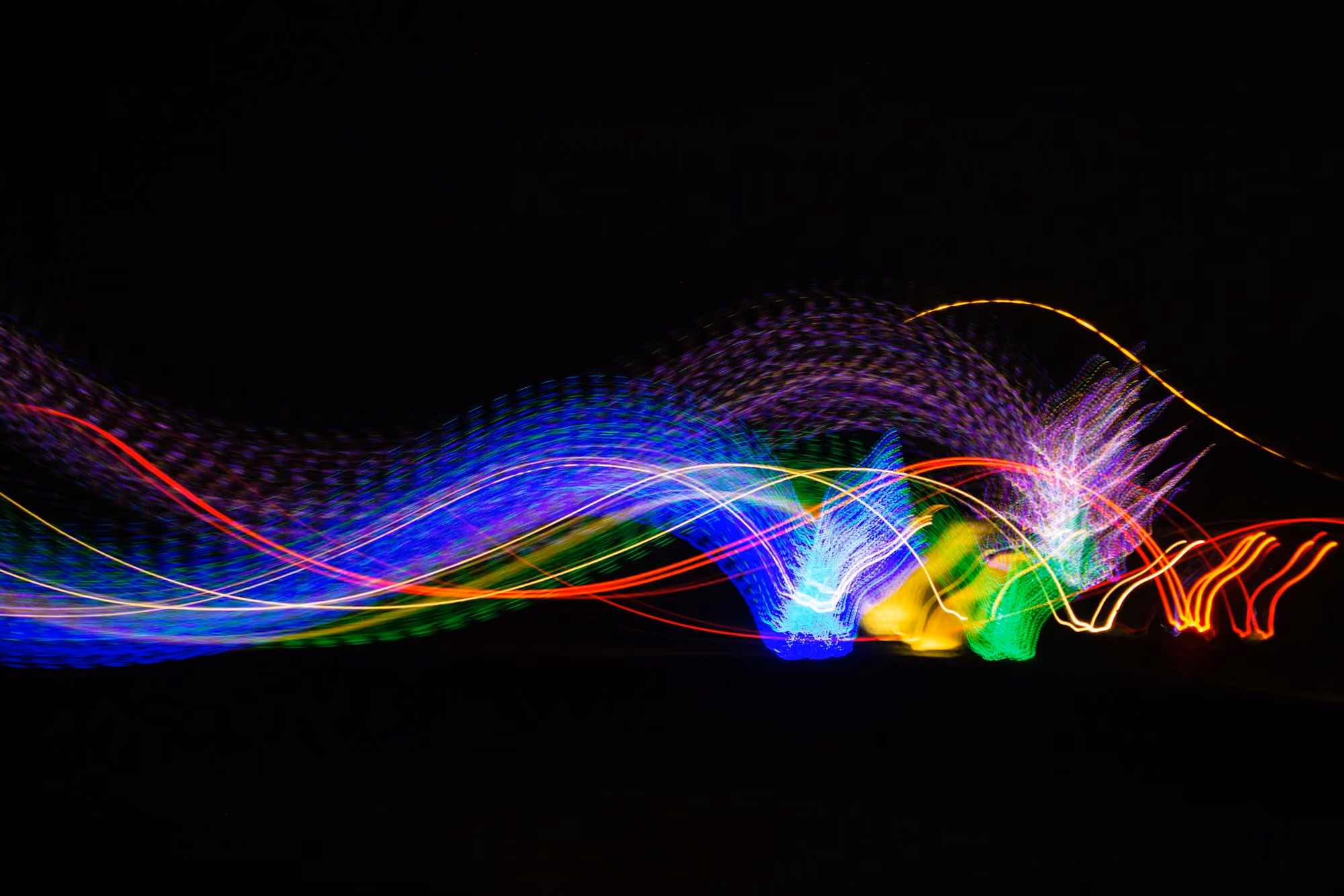 Colorful abstract light trails in blue, green, yellow, red, and purple on a black background.