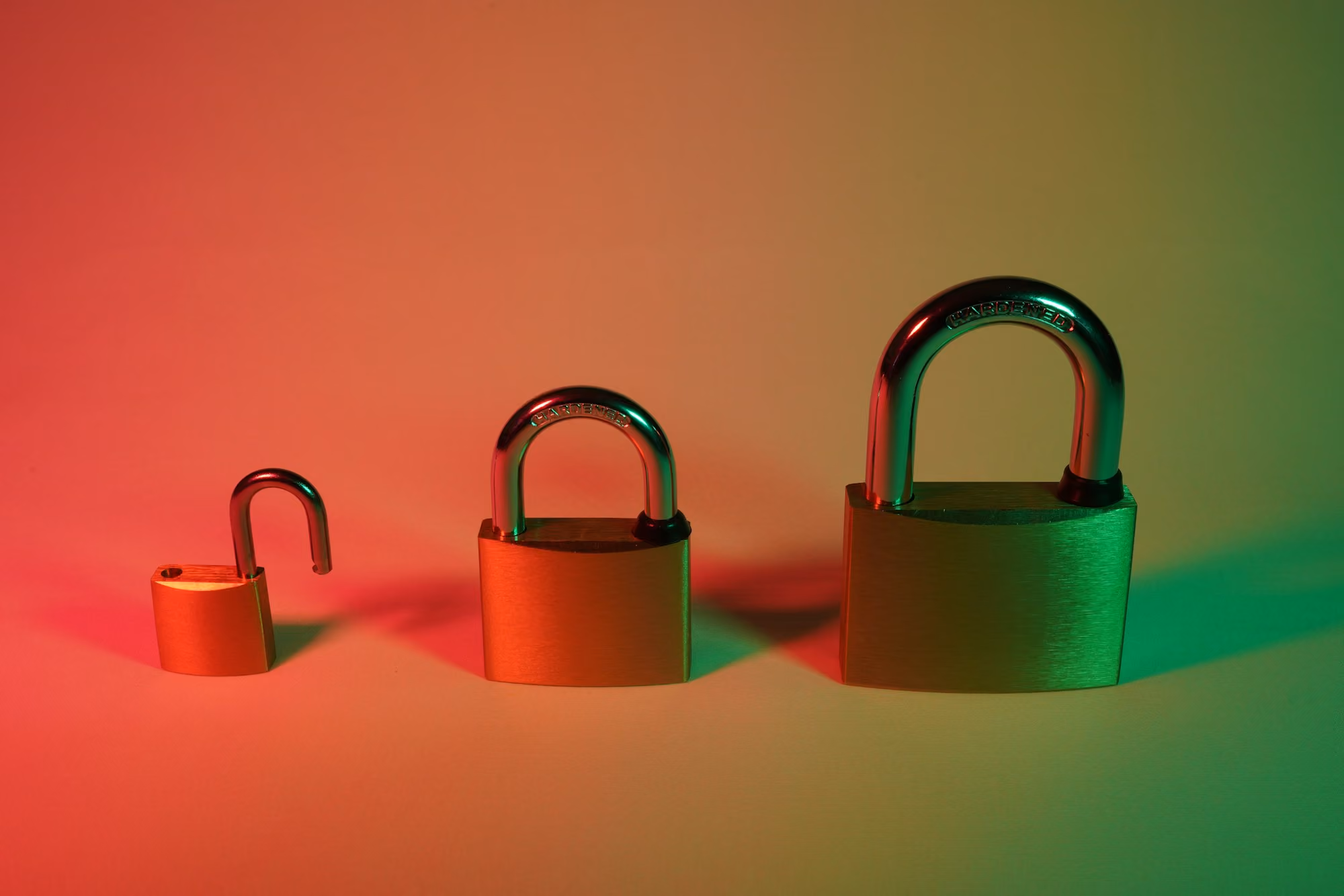 Three padlocks of varying sizes, smallest unlocked and others locked, lit with red and green light.