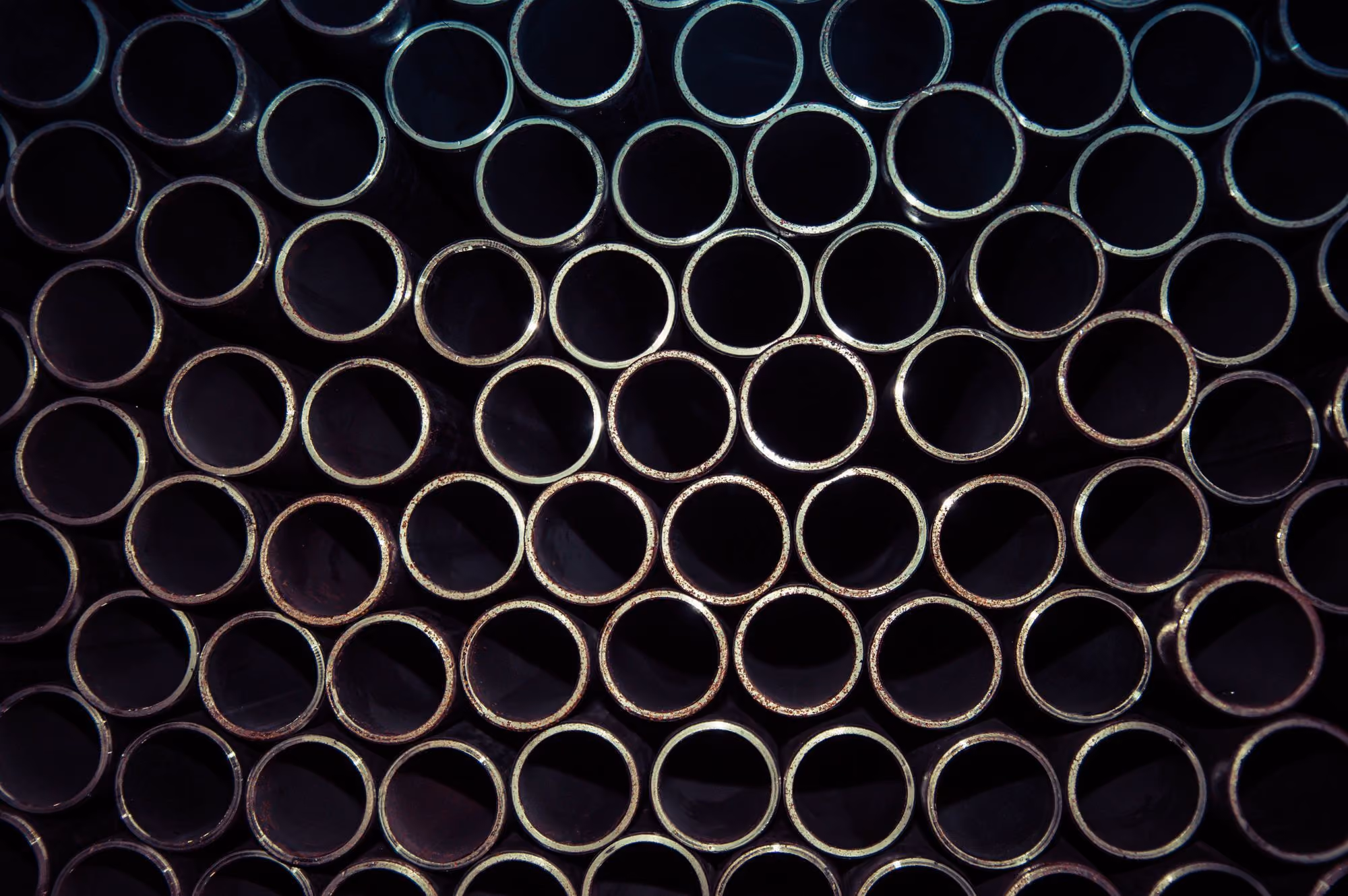 Close-up of stacked metallic pipes showing their circular open ends in a grid pattern.
