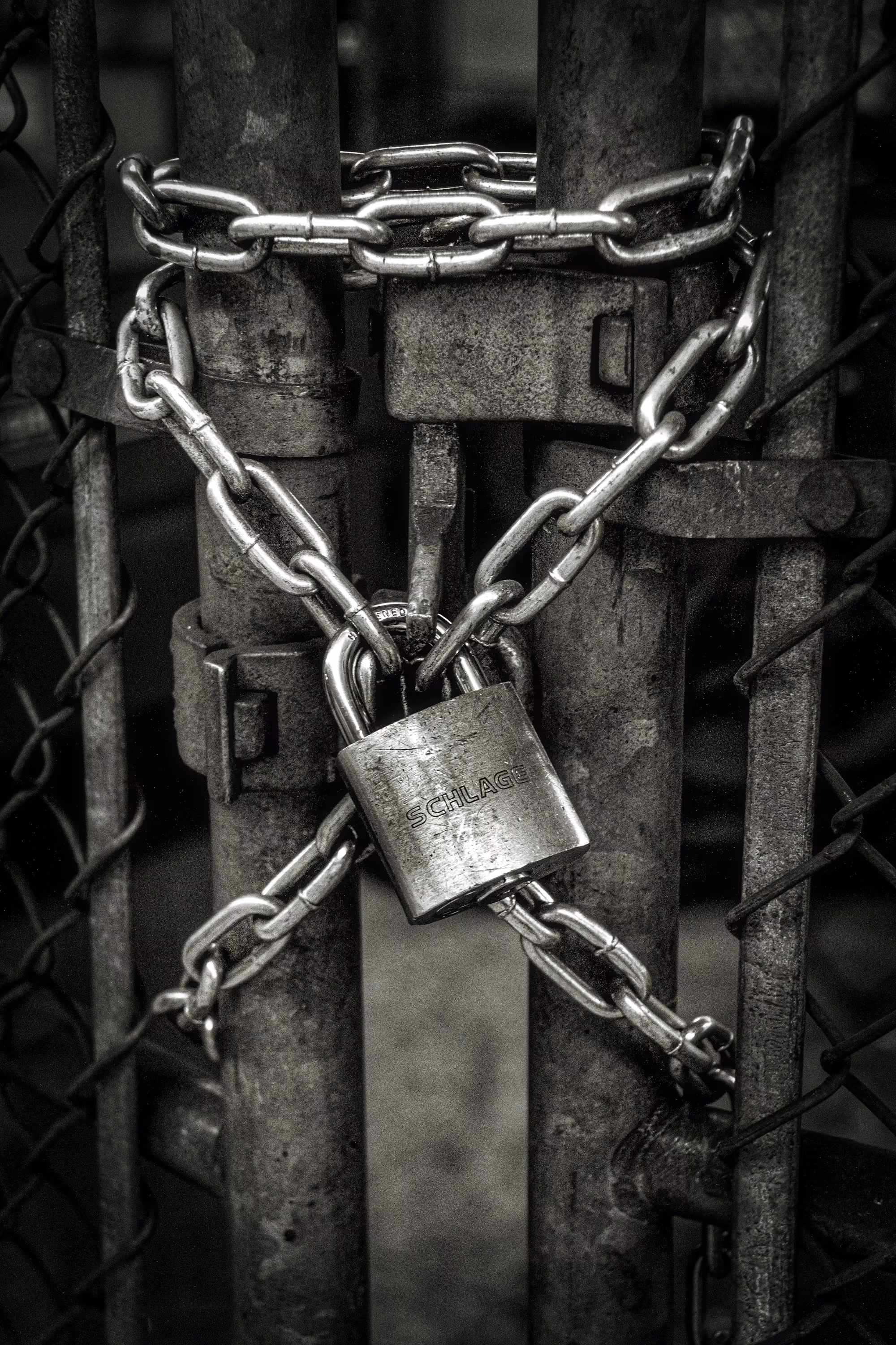 Rusty metal gate secured with a chain and a Schlage padlock in black and white.