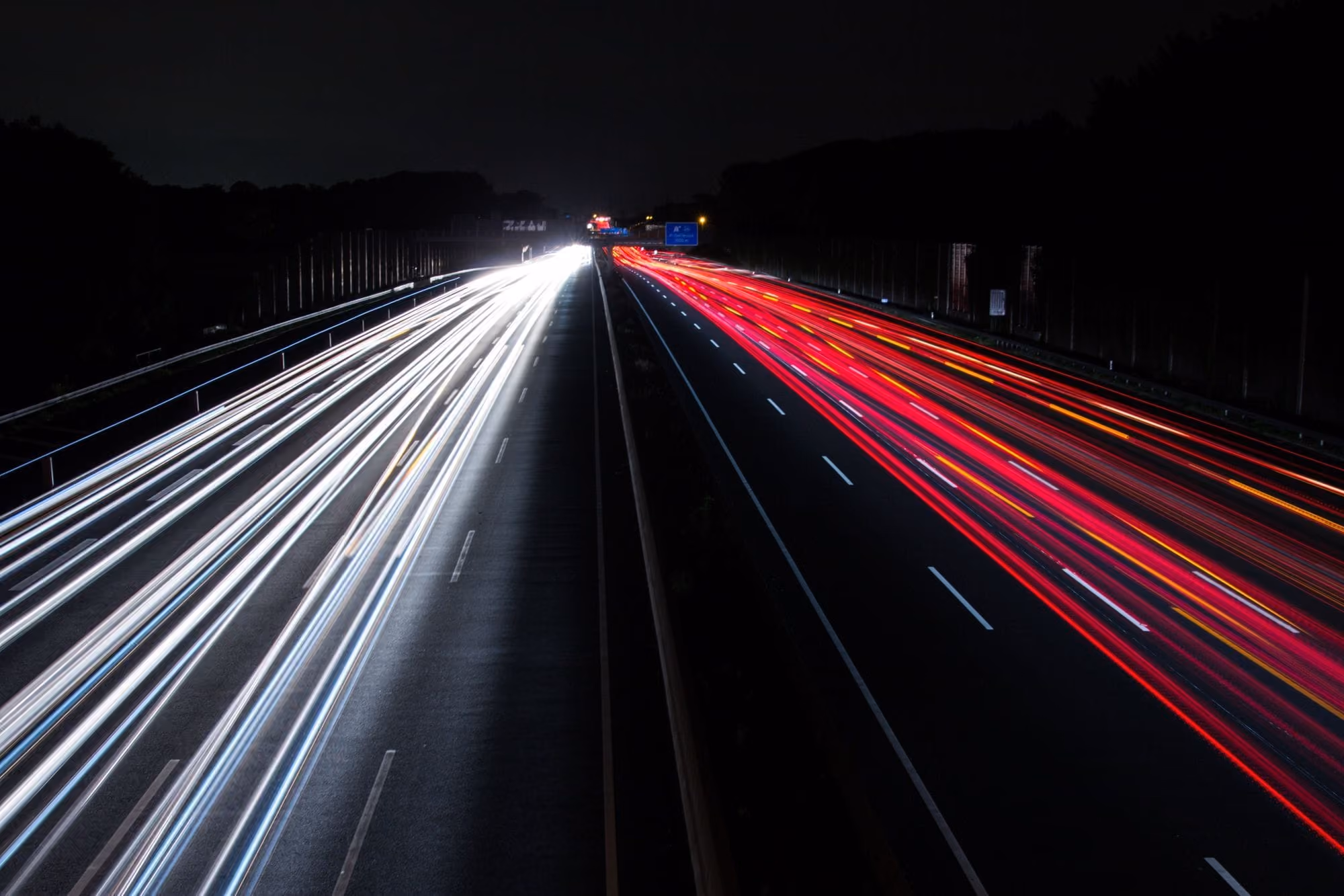 Highway at night with long exposure showing white and red light trails of moving vehicles.