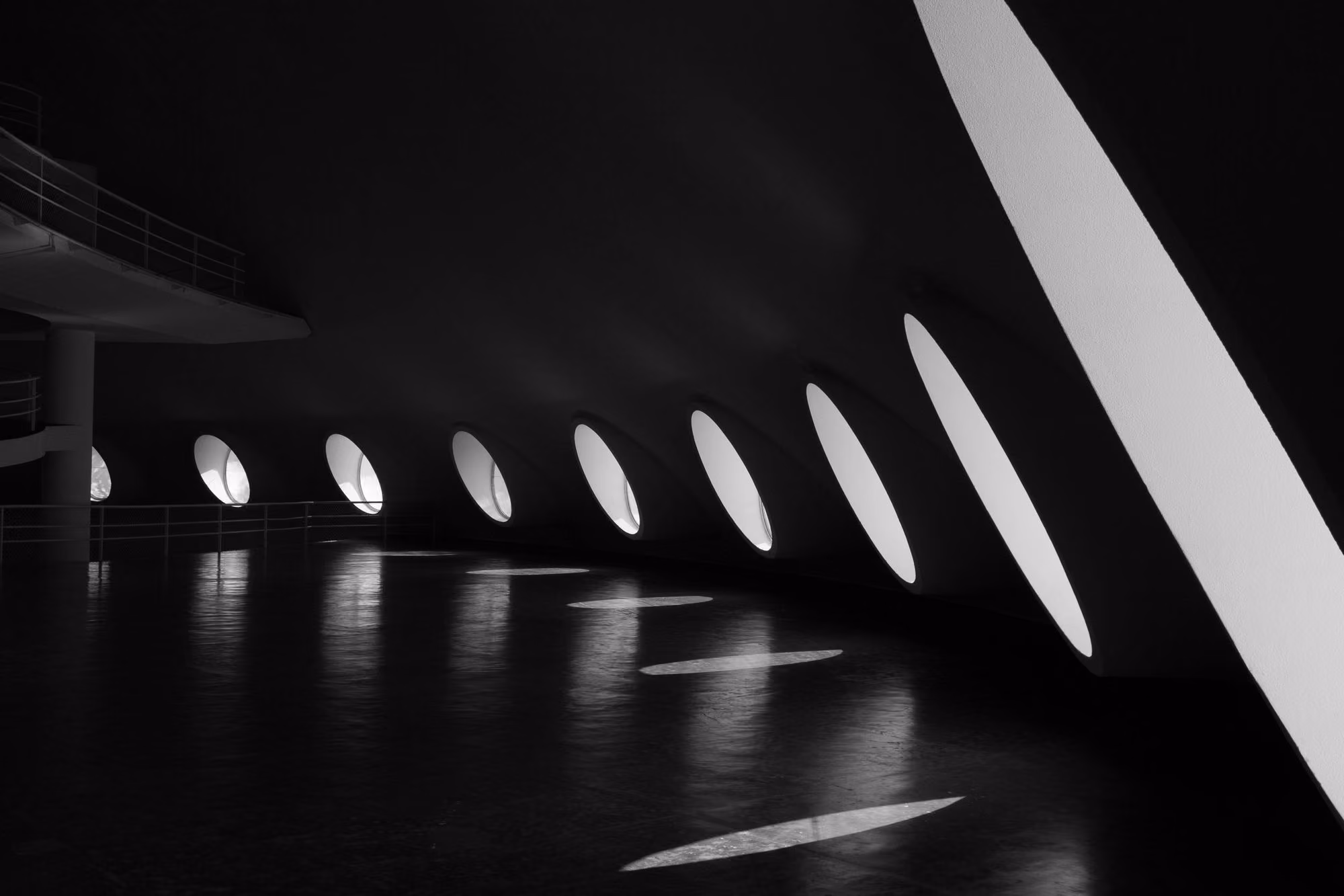 Black and white photo of light streaming through oval windows casting shapes on a dark floor.