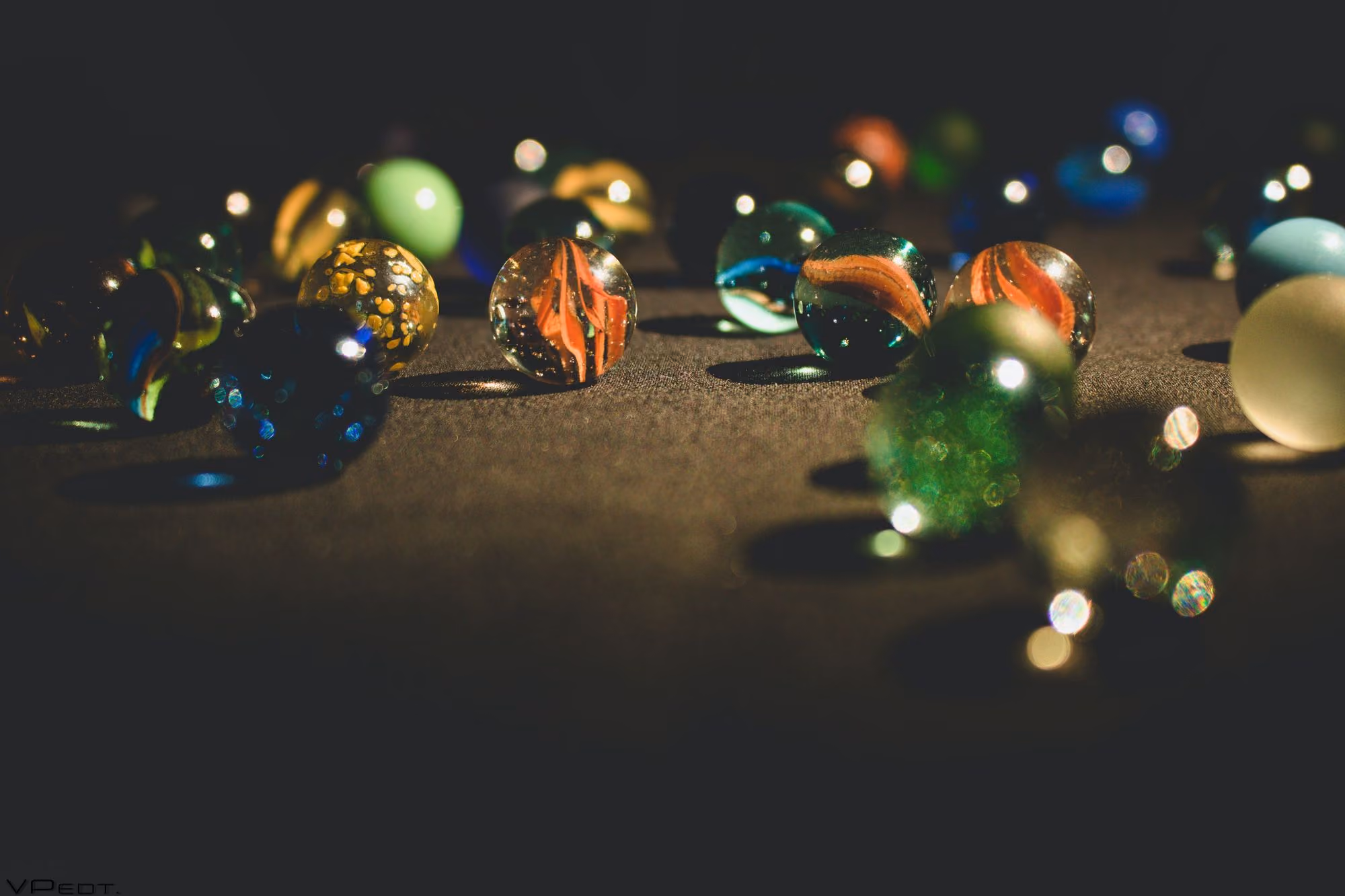 Close-up of colorful glass marbles scattered on a dark surface with soft lighting and shadows.