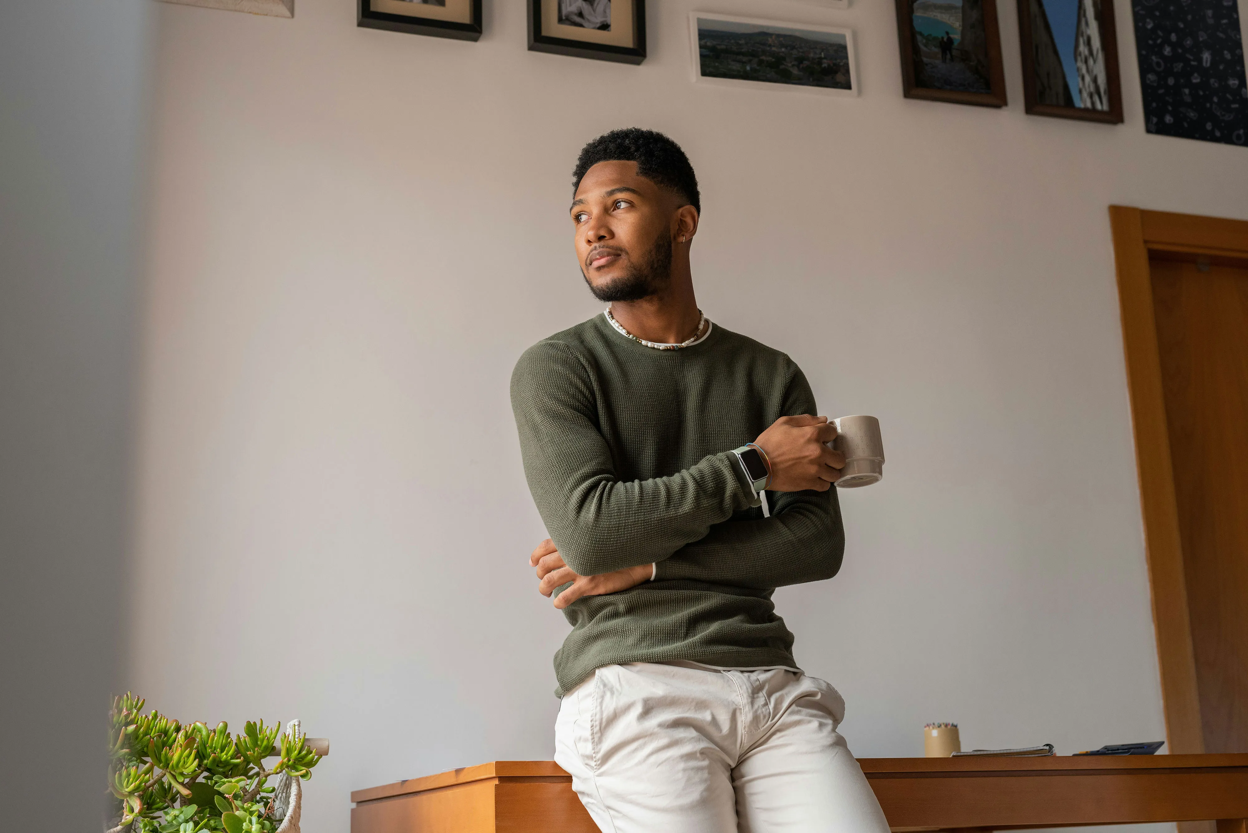 Person holding coffee mug, leaning against desk with framed artwork behind