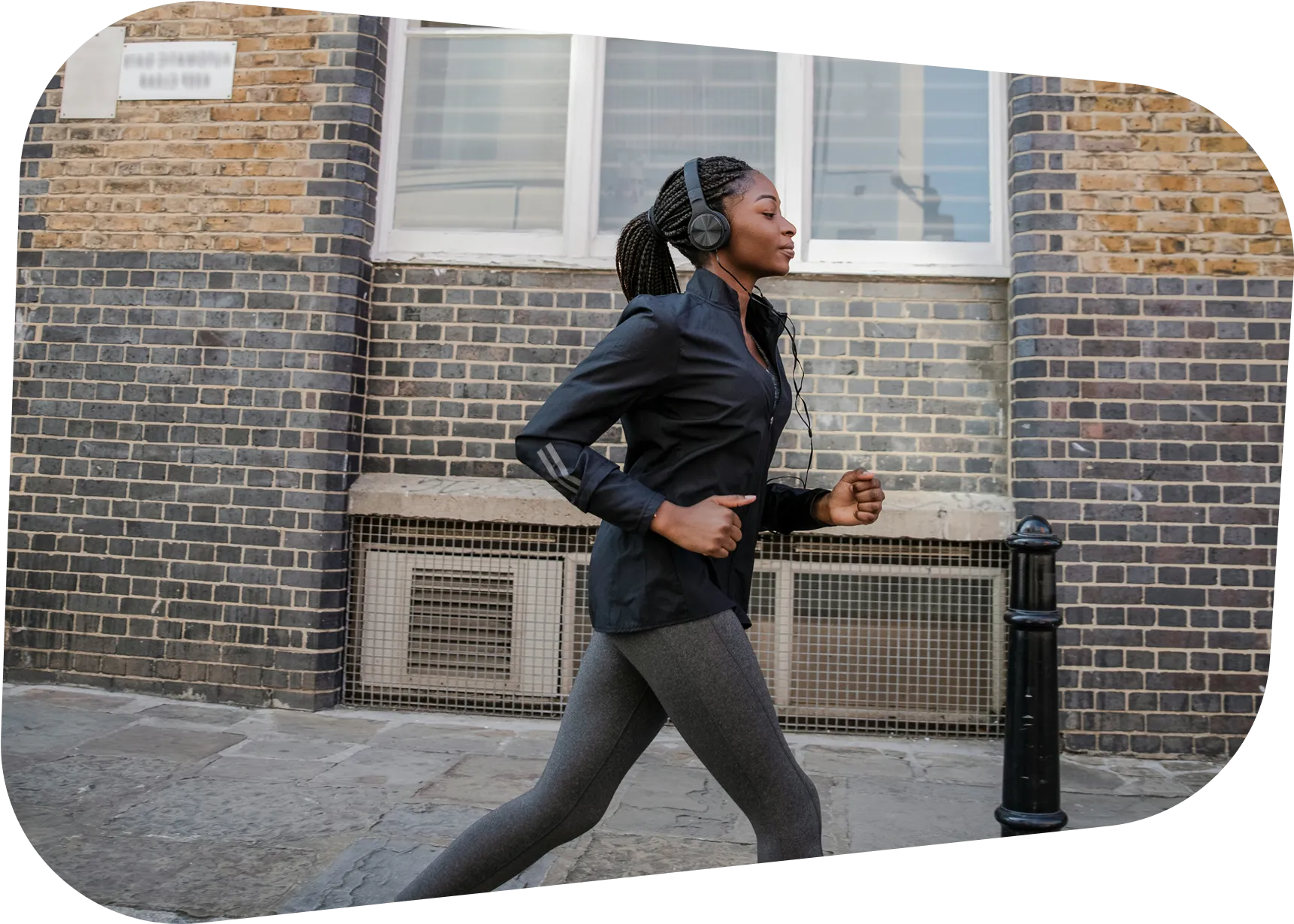 Woman jogging in urban setting with headphones, wearing black jacket