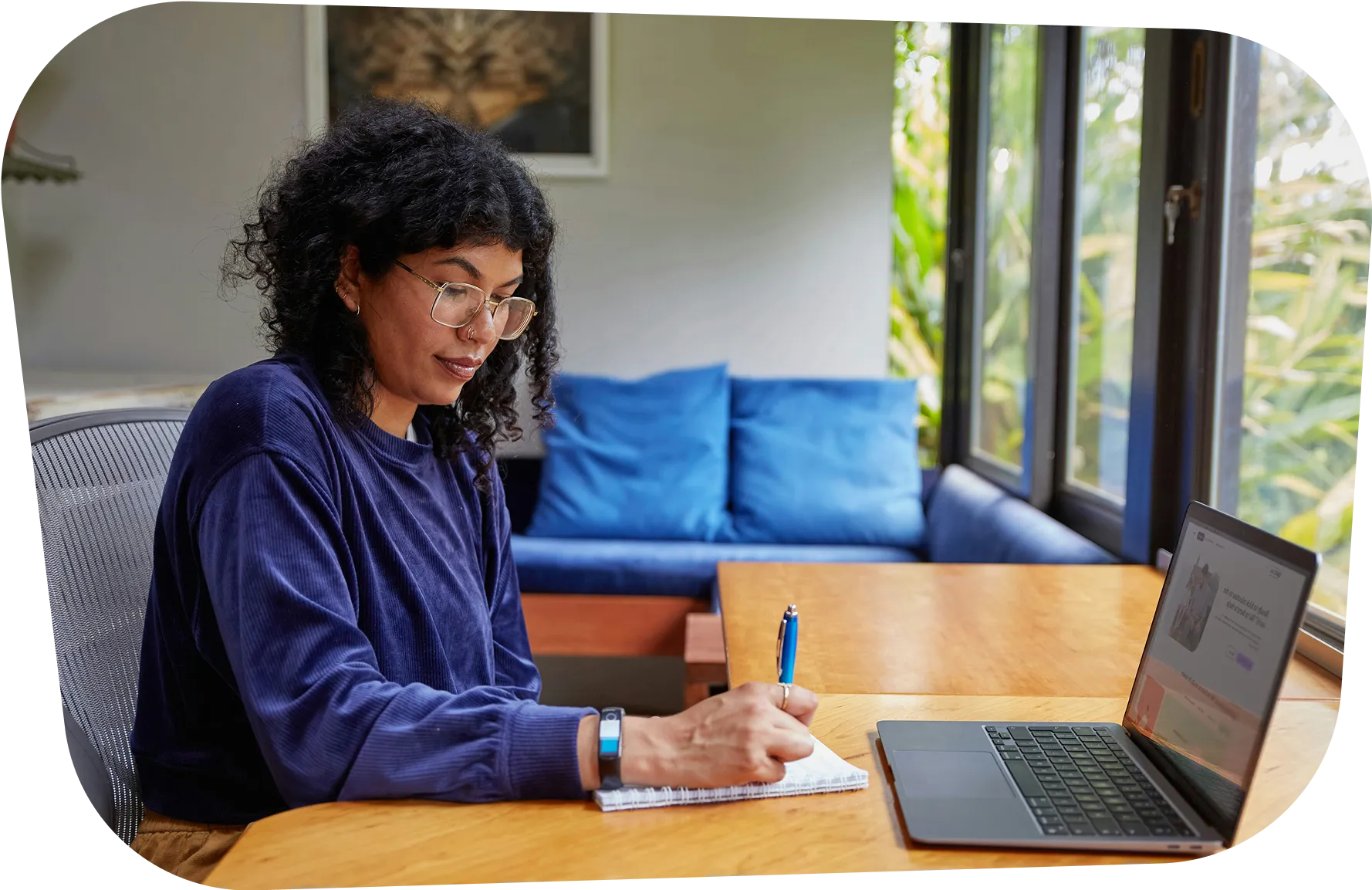 Woman in blue sweater studying with laptop and notebook by window