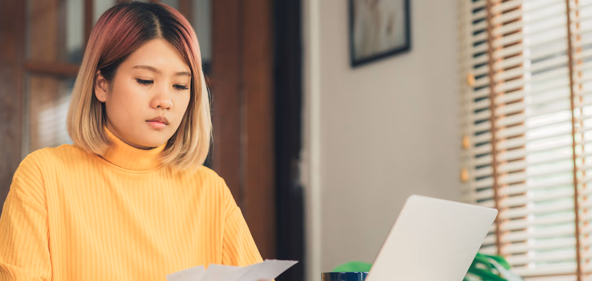 Woman in yellow sweater working on laptop near window