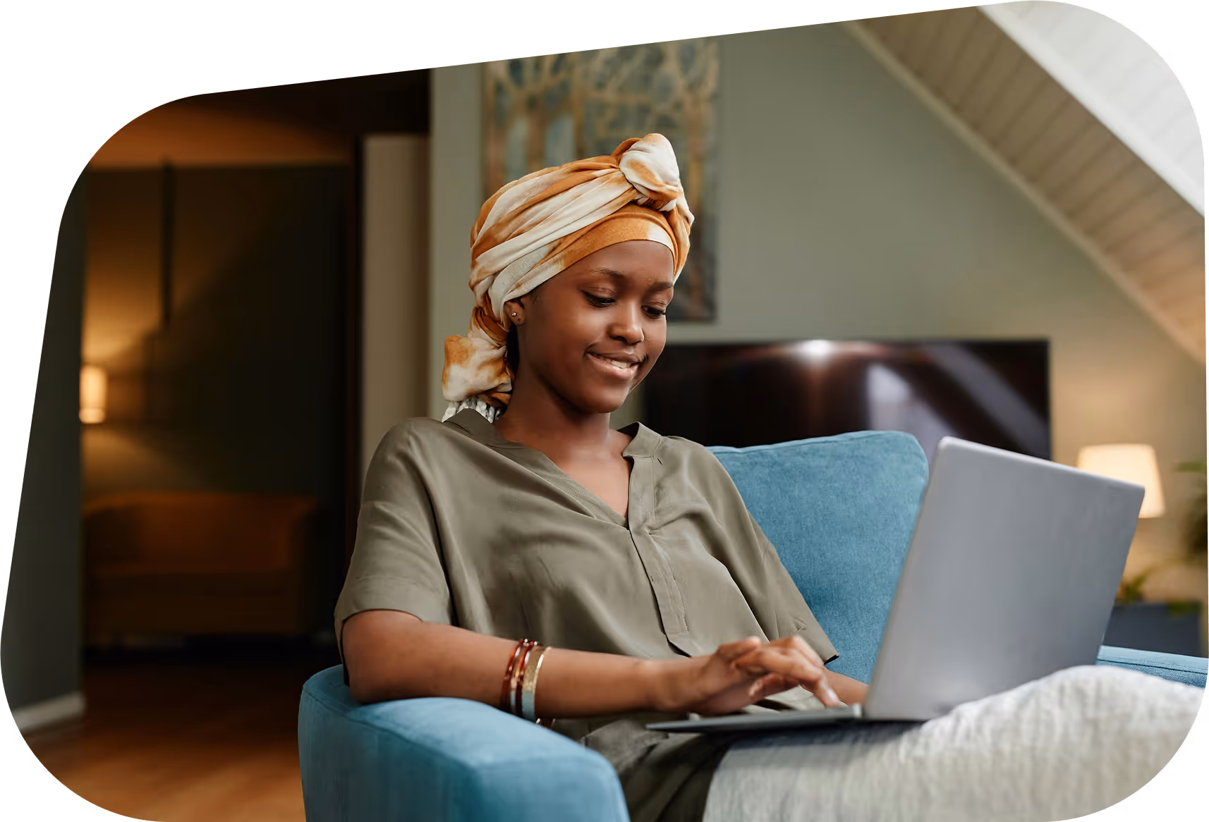 Woman in headwrap working on laptop at home, sitting on blue chair