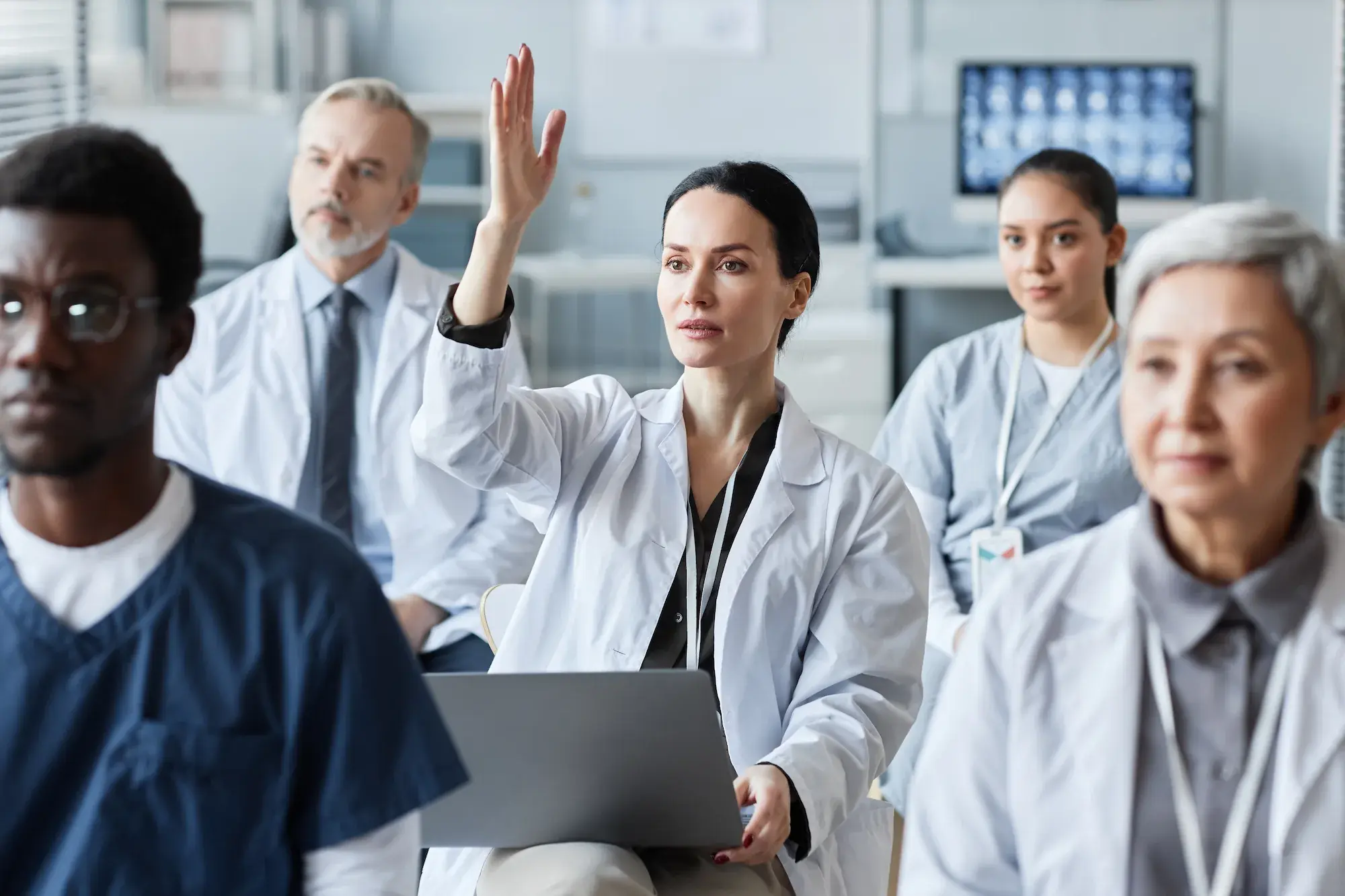 A brunette general practitioner raising her hand in a meeting.