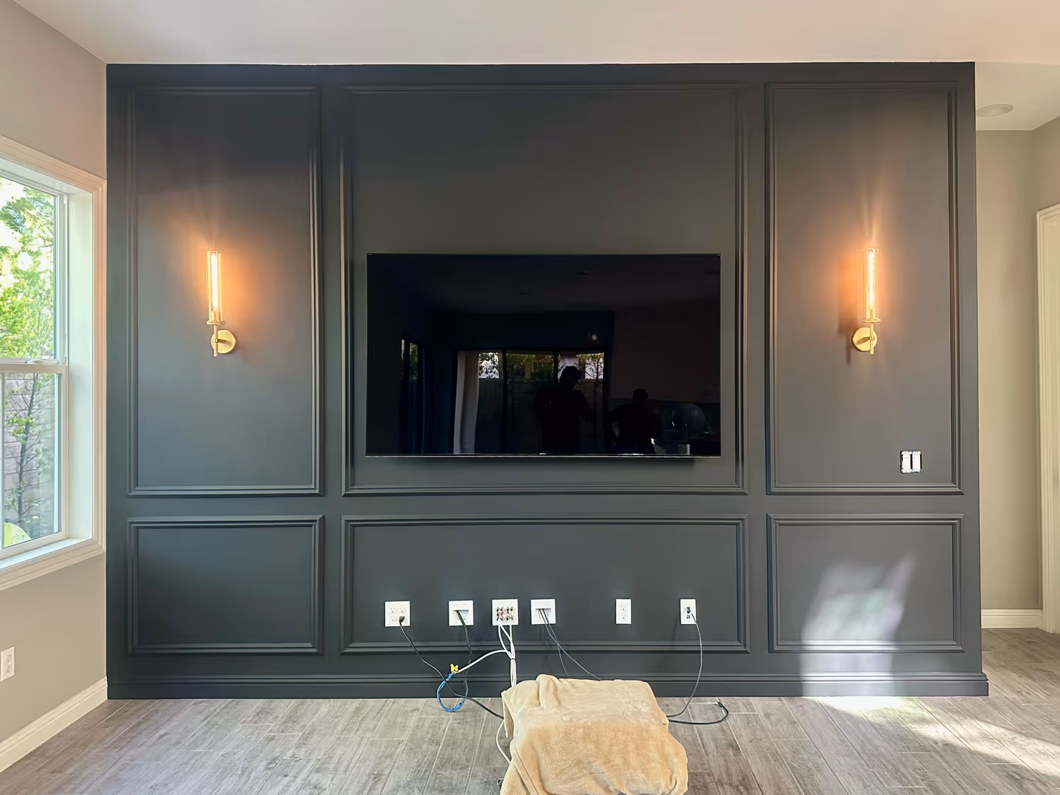 Black accent wall with inset TV, decorative molding, and brass sconces. Modern luxury wall design in Orange County.