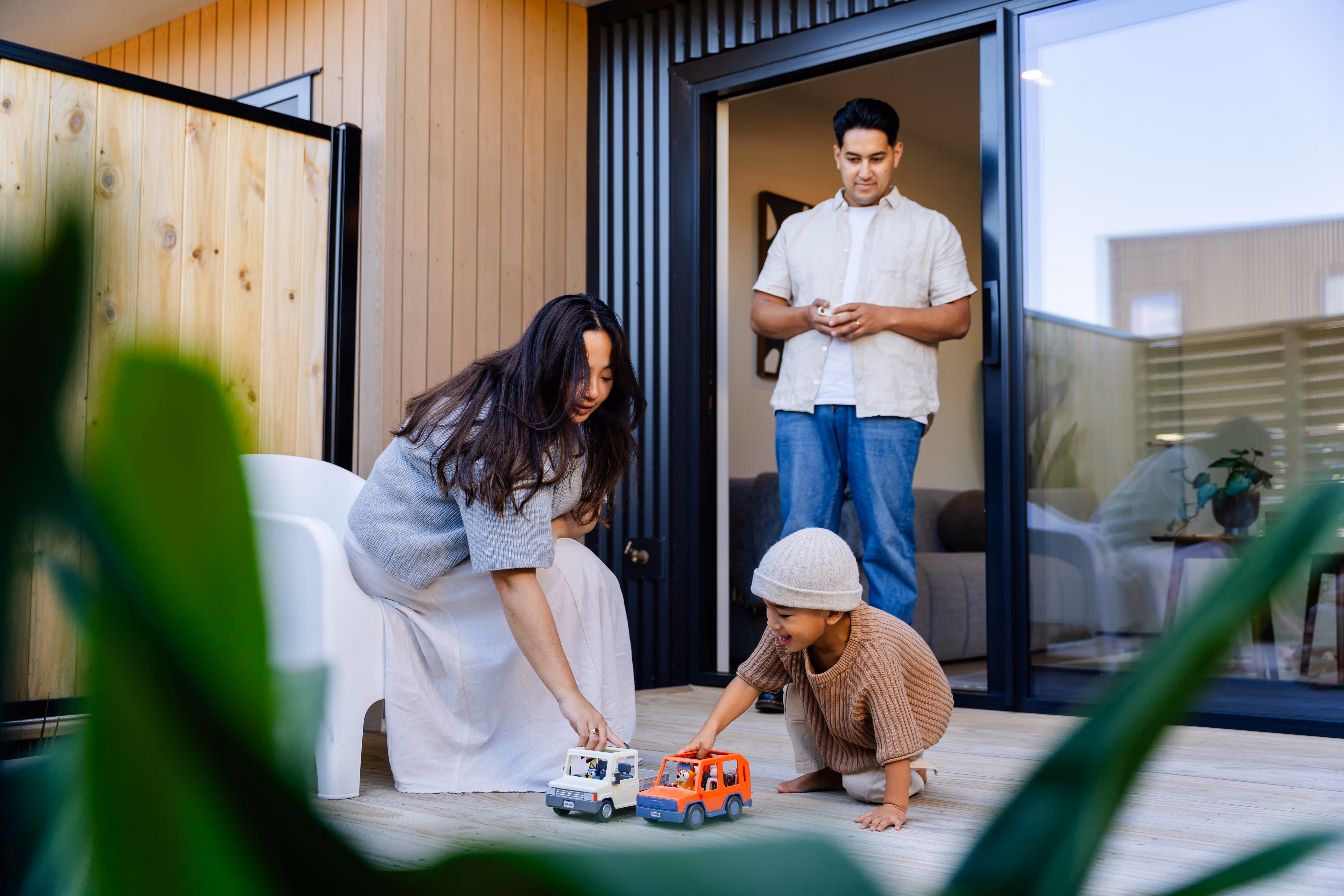 Contemporary family home with seamless indoor-outdoor living, parents and young child enjoying deck space with natural wood and black frame architecture