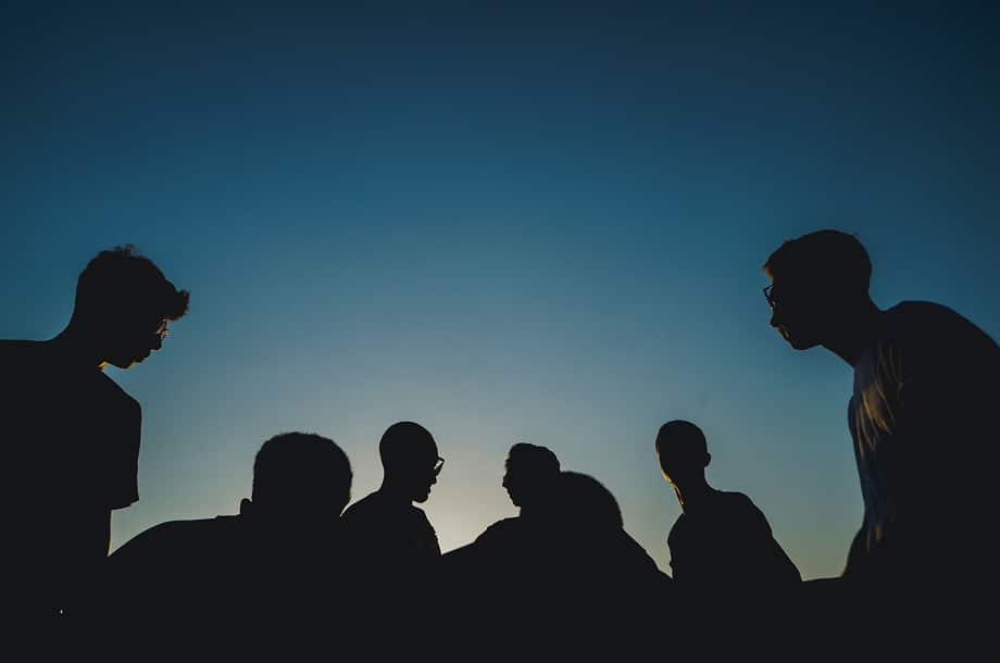 Silhouettes of seven people against a clear sky at sunset or sunrise.