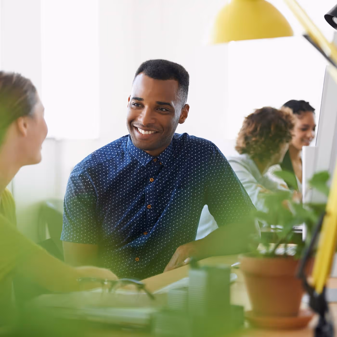 Smiling man in a blue shirt talking with a colleague in a bright office space.