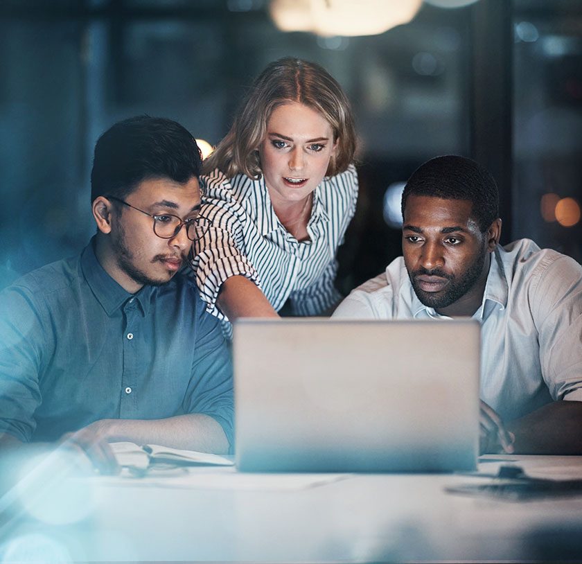 Three colleagues, a woman and two men, looking carefully at an unobserved laptop screen.