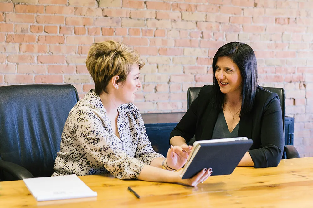 Two women looking at a tablet in an office setting.