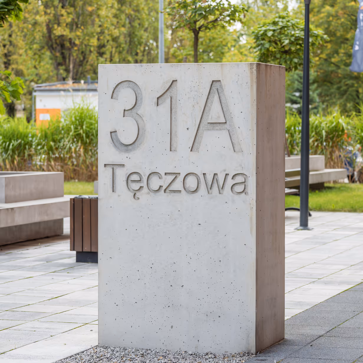 Betonowy monolit z adresem 31A Tęczowa w nowoczesnym parku