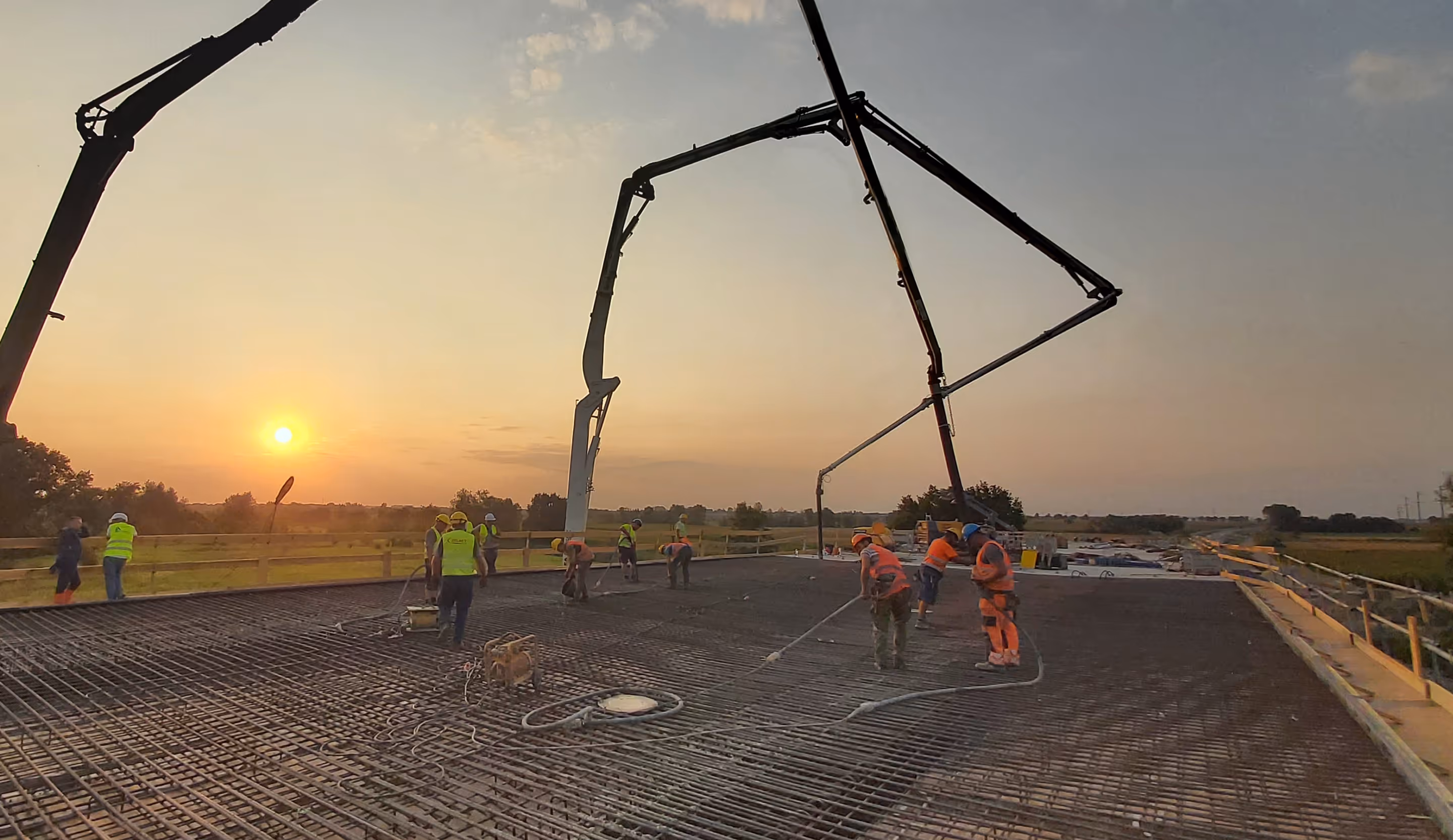 Robotnicy budowlani leją beton na konstrukcję mostu o zachodzie słońca